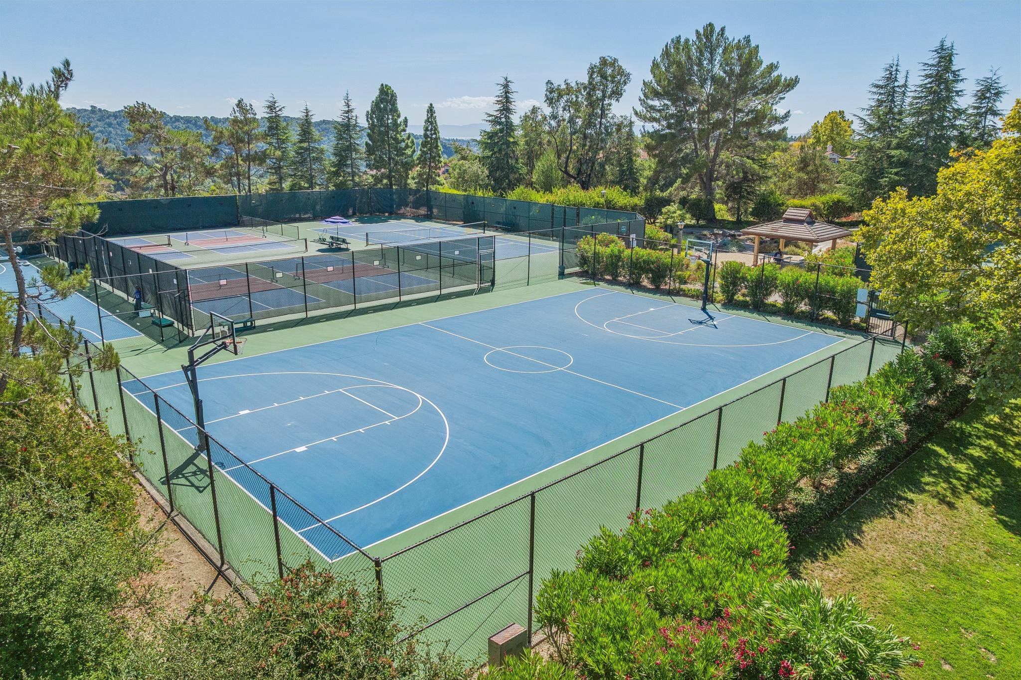 Outdoor tennis courts surrounded by lush greenery and tall trees, with a gazebo and mountain view in the background.