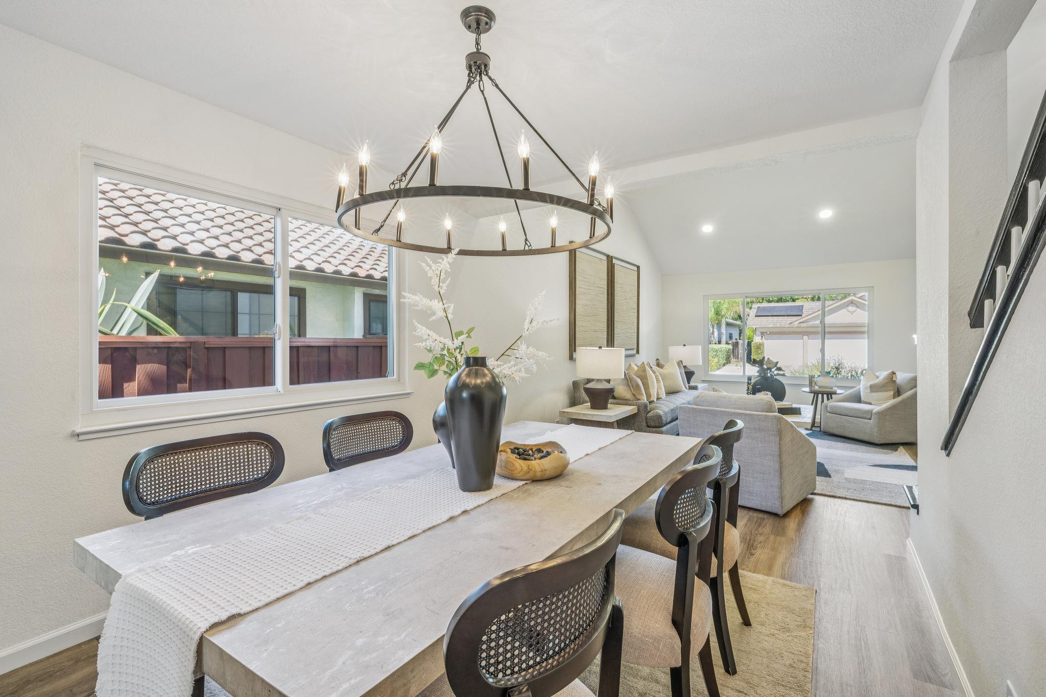 Open-concept living and dining room with large windows, a chandelier, and neutral-colored furniture.
