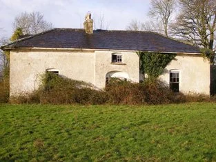 An old, weathered house with a dark roof, ivy growing on the side, and a grassy foreground.