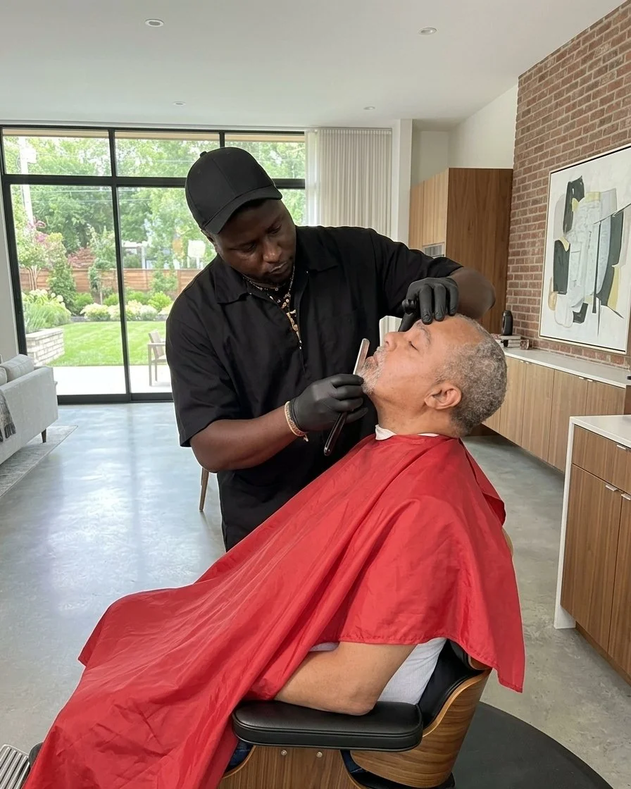 A barber giving an elderly man a shave in a modern, well-lit salon with large windows and a view of a garden.