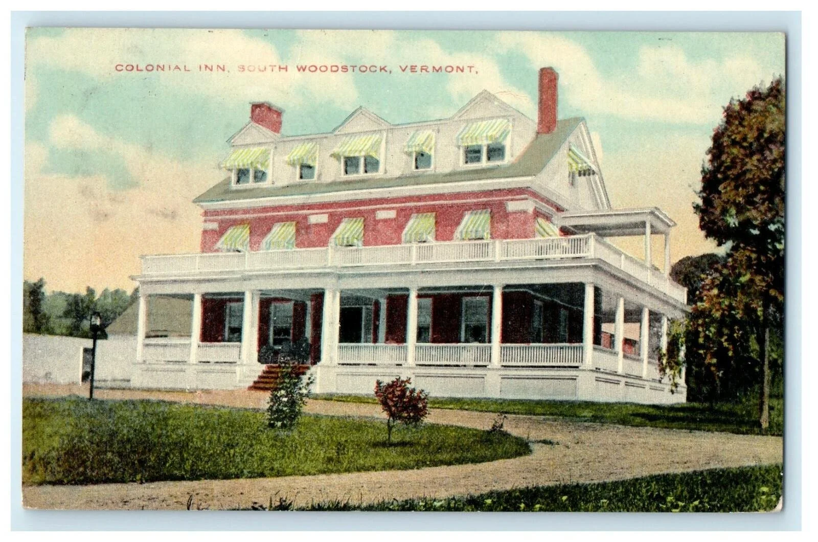 Colorized vintage postcard of a large, multi-story white house with red brick sections, green and white striped awnings, and a wraparound porch at Colonial Inn in South Woodstock, Vermont, surrounded by a garden and a dirt pathway.