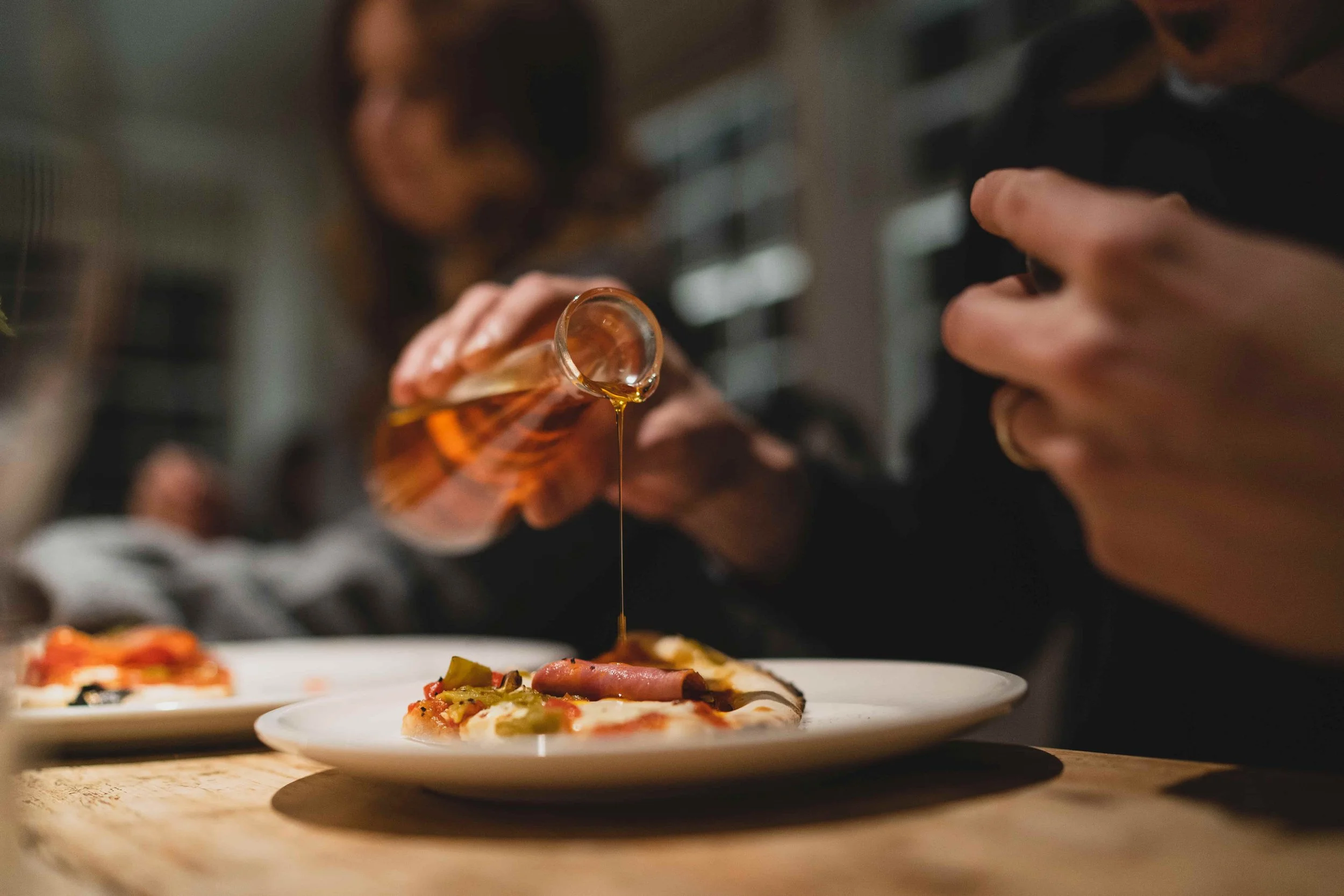 Person pouring honey onto pizza slices at a dining table.