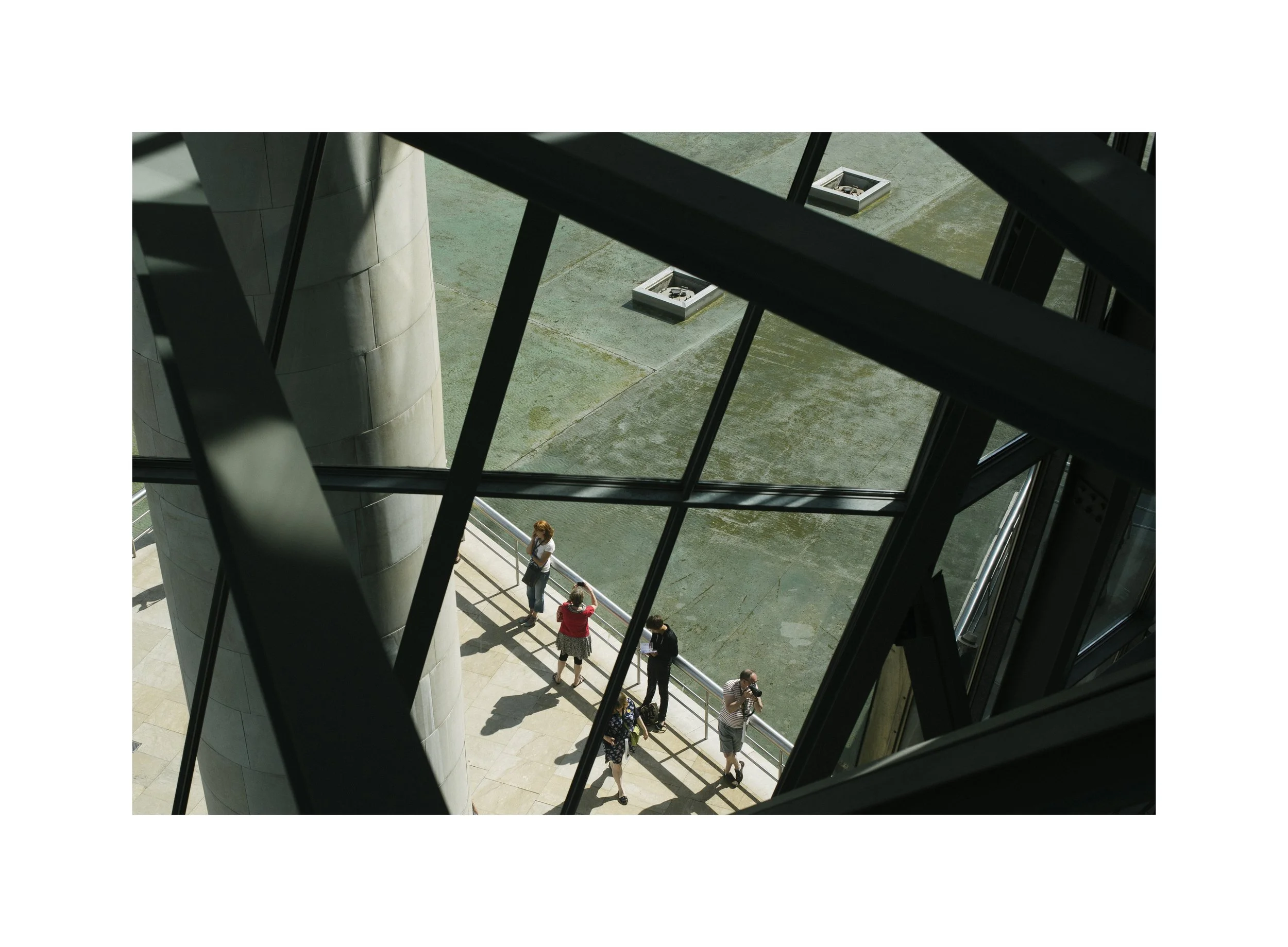 Vue depuis le sommet d'un bâtiment montrant des gens en bas, vus à travers une structure en métal avec des panneaux de verre.