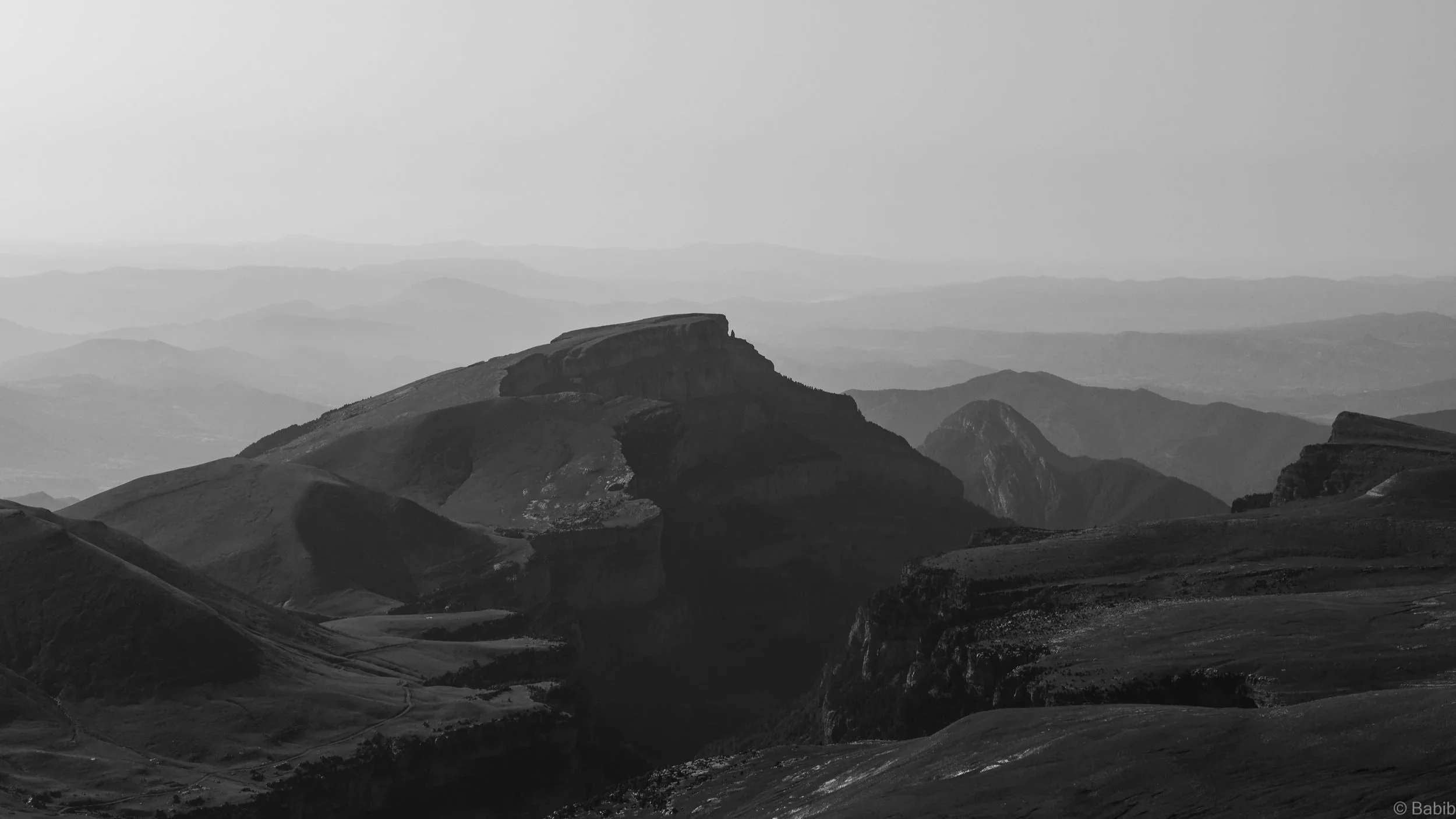 Paysage de montagnes rocheuses en noir et blanc, with multiple couches de montagnes s'étendant vers l'horizon.