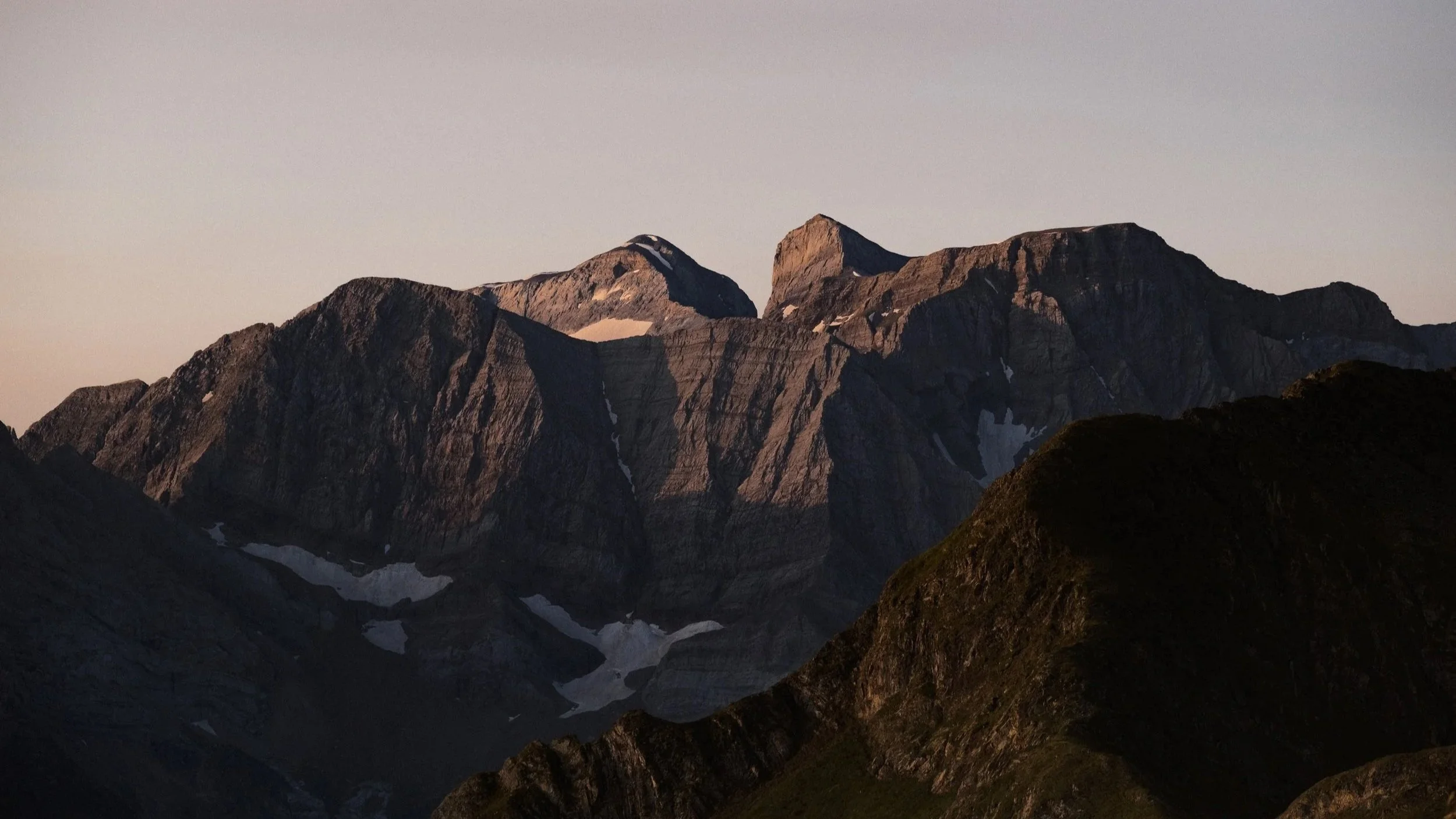 Montagnes rocheuses avec sommets enneigés au crépuscule ou au lever du soleil, ciel clair.
