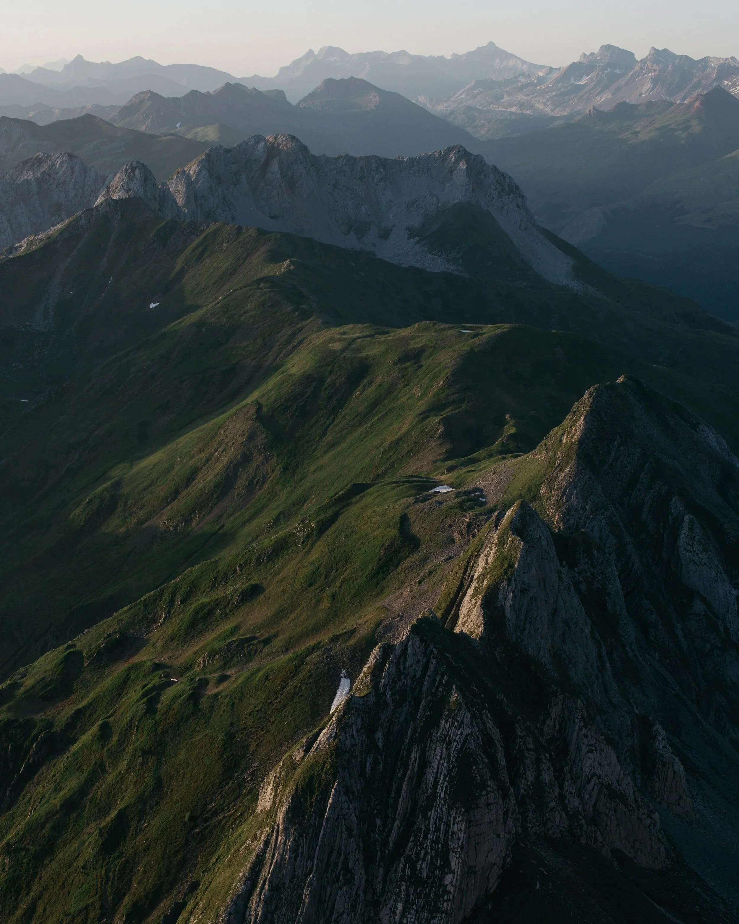 Paysage de montagnes avec des sommets rocheux et des versants recouverts d'herbe, sous un ciel clair.