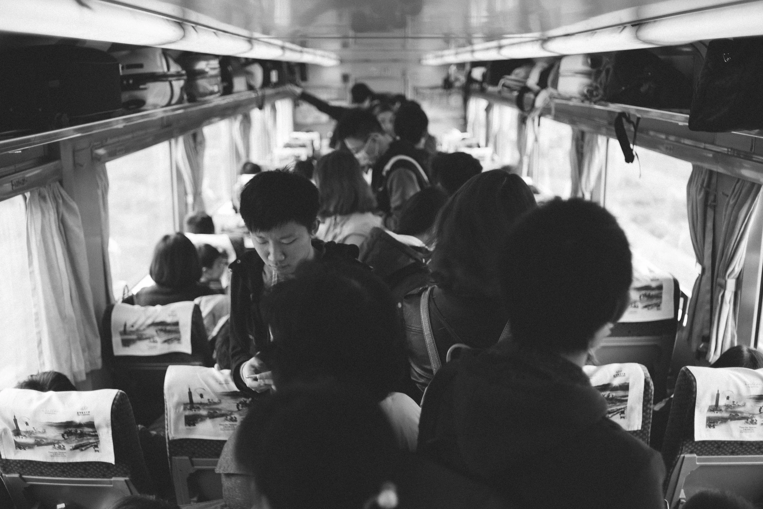 Voyage en bus avec plusieurs passagers assis, certains regardant vers le bas, dans un intérieur de bus avec fenêtres et rideaux.
