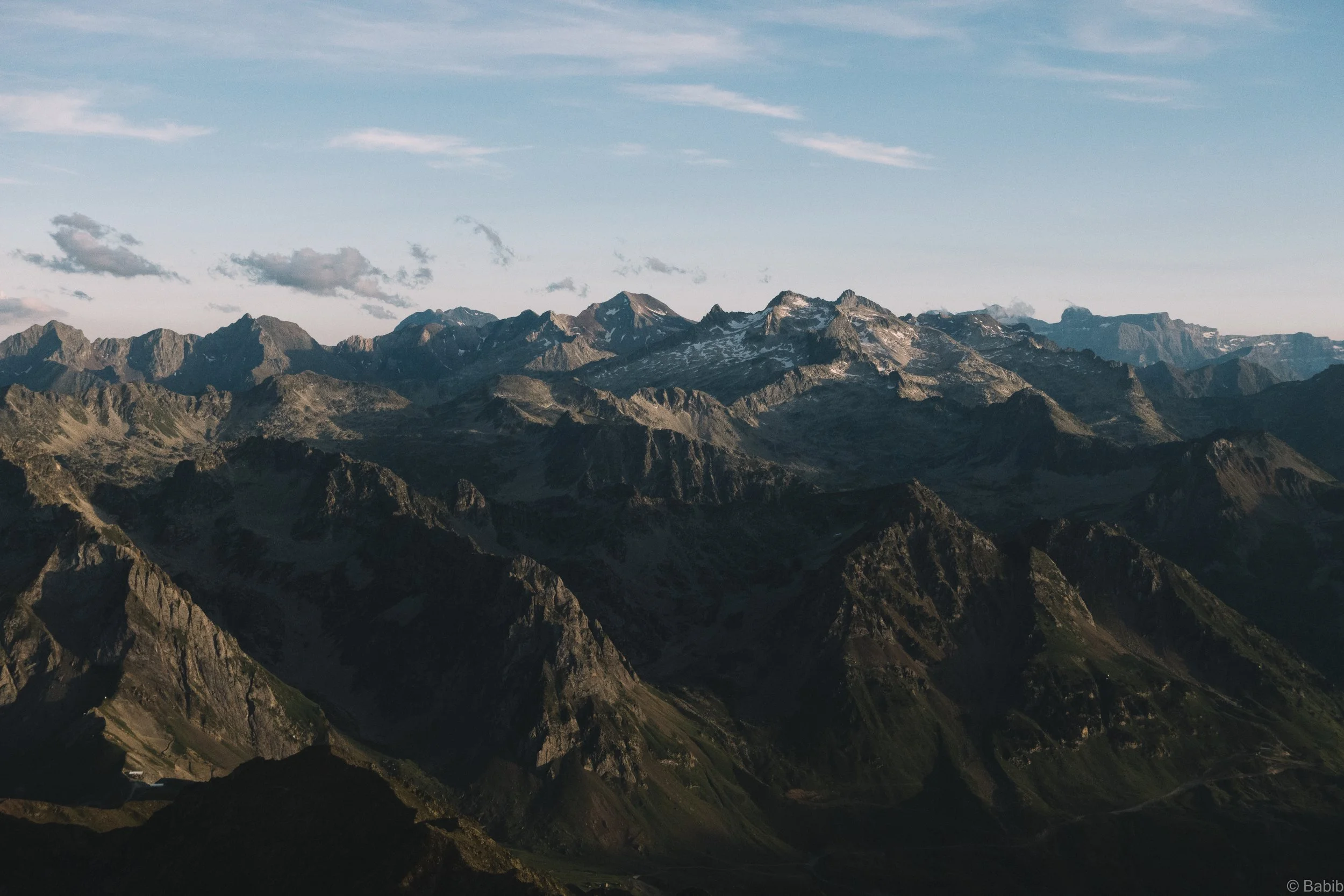 Une chaîne de montagnes rocheuses sous un ciel bleu avec quelques nuages.