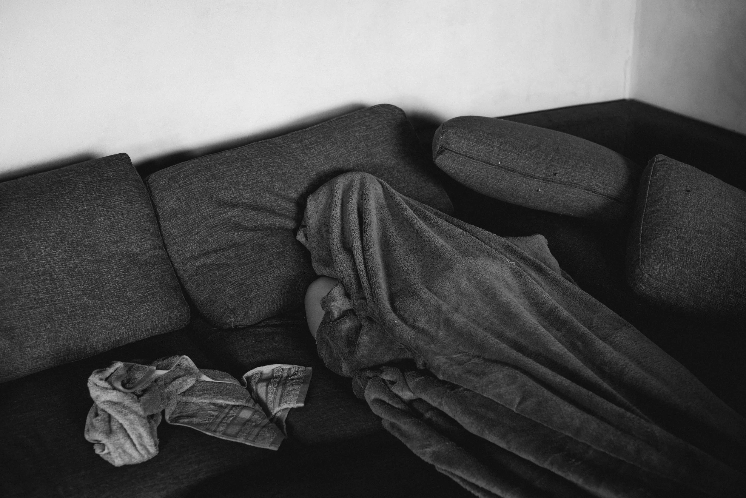 Un canapé gris avec des coussins, recouvert d'une couverture, dans une pièce aux murs blancs.