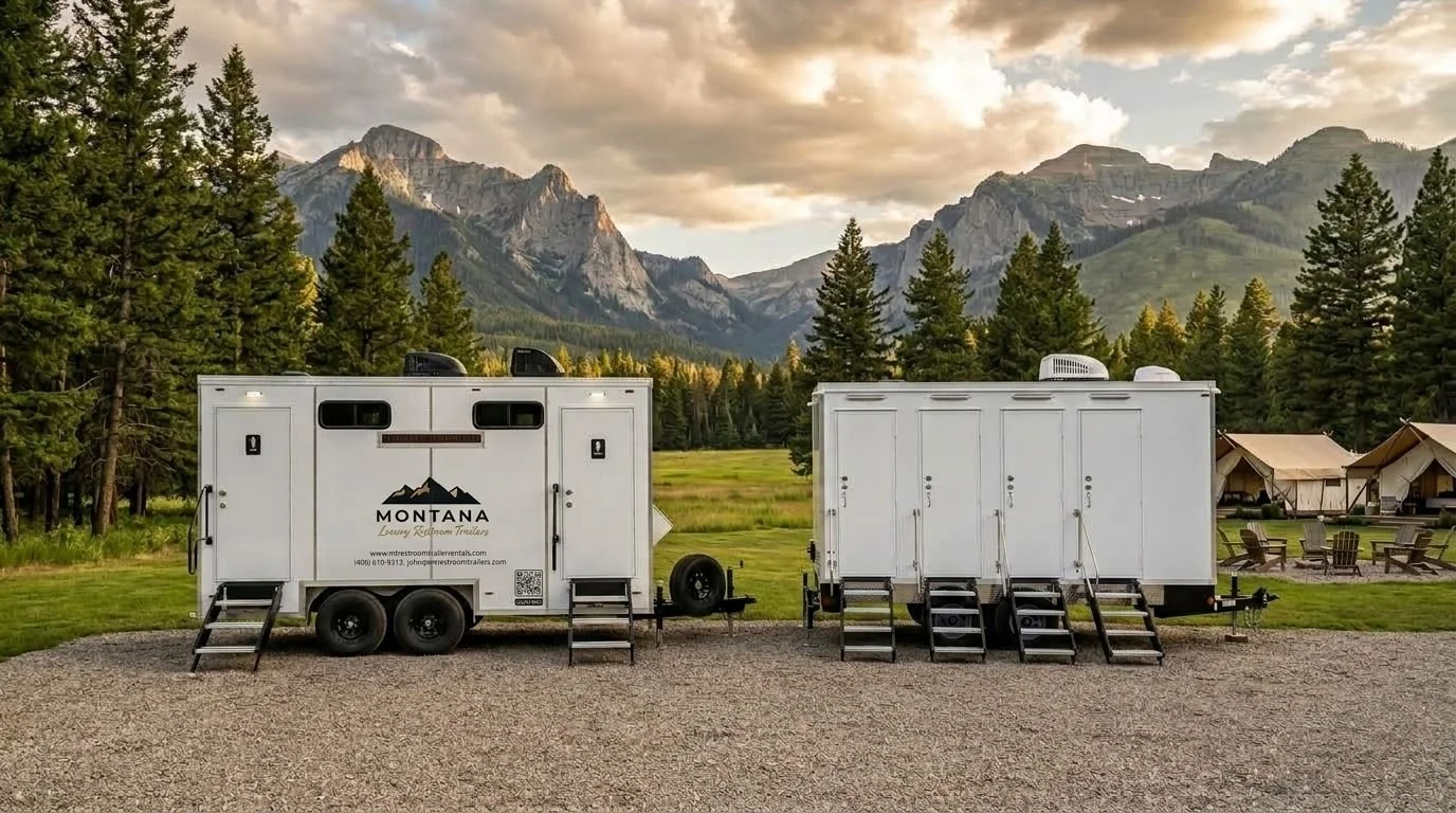Two white mobile trailers with black steps, set against a scenic mountain landscape with pine trees, tents, and outdoor chairs.
