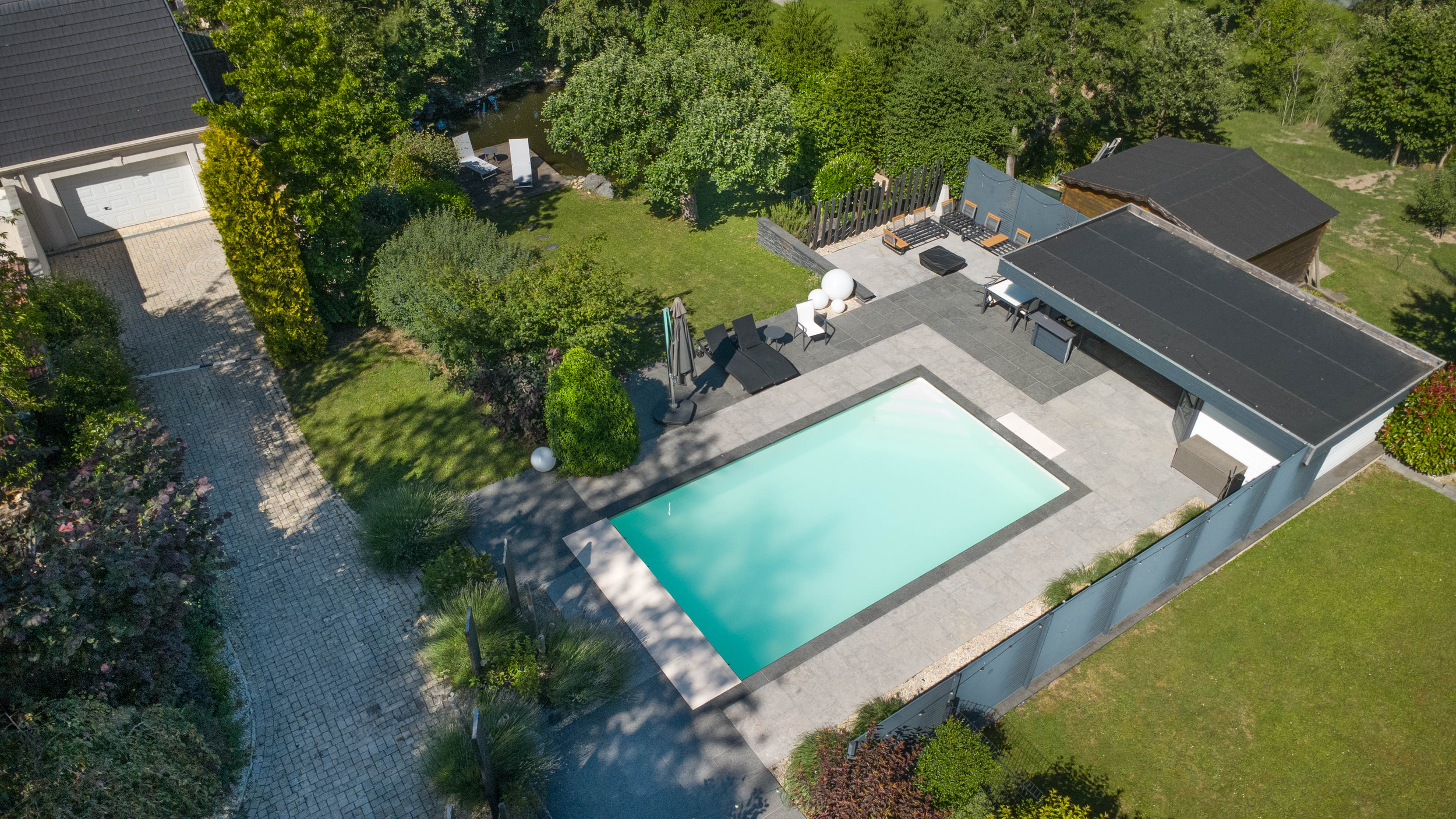 VUE AÉRIENNE D'UNE PISCINE ET D'ESPACE EXTÉRIEUR AUTOUR D'UNE MAISON, entouré d'arbres et de pelouses.