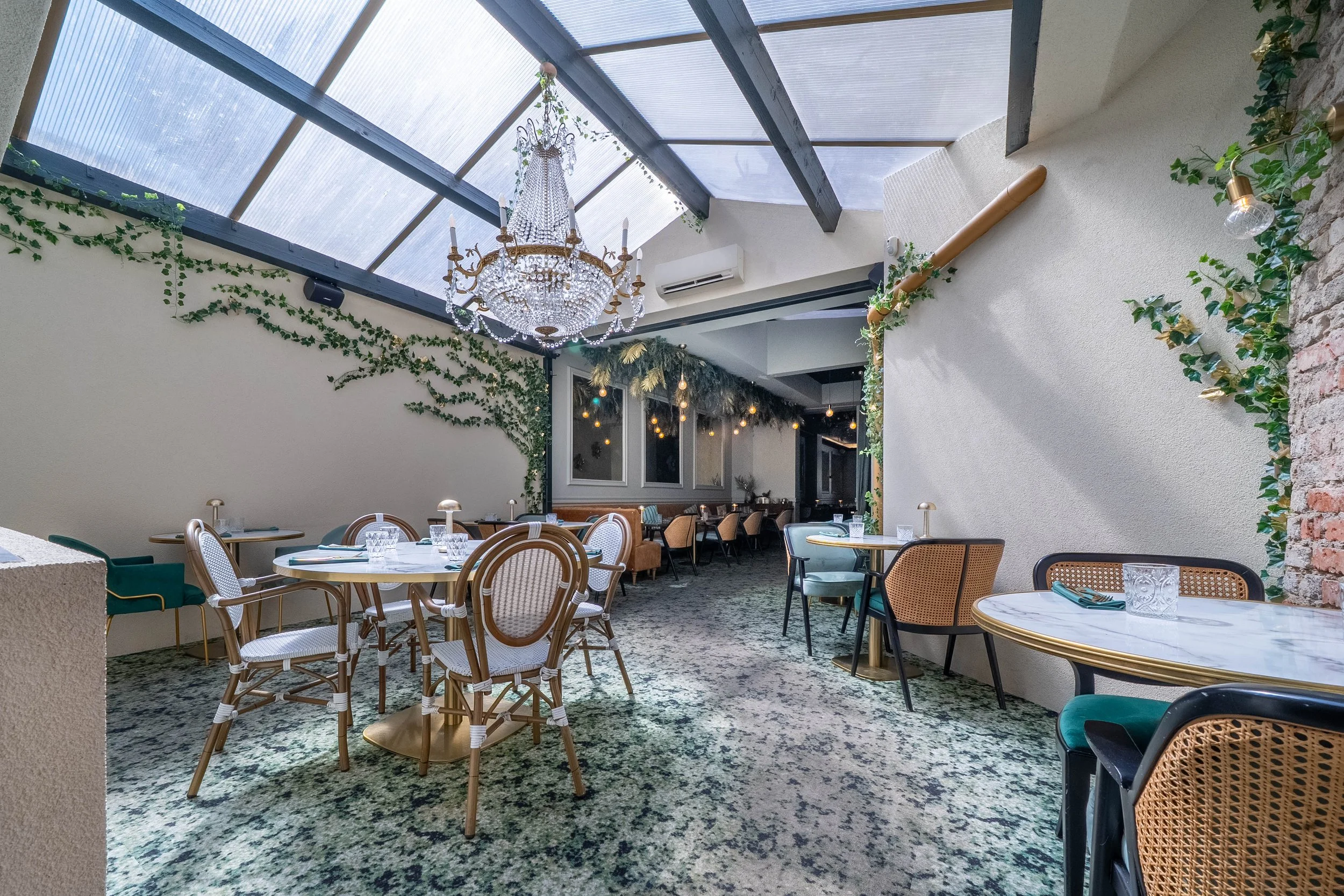Salle à manger intérieure avec plafond en verre, chandelier et décorations végétales.