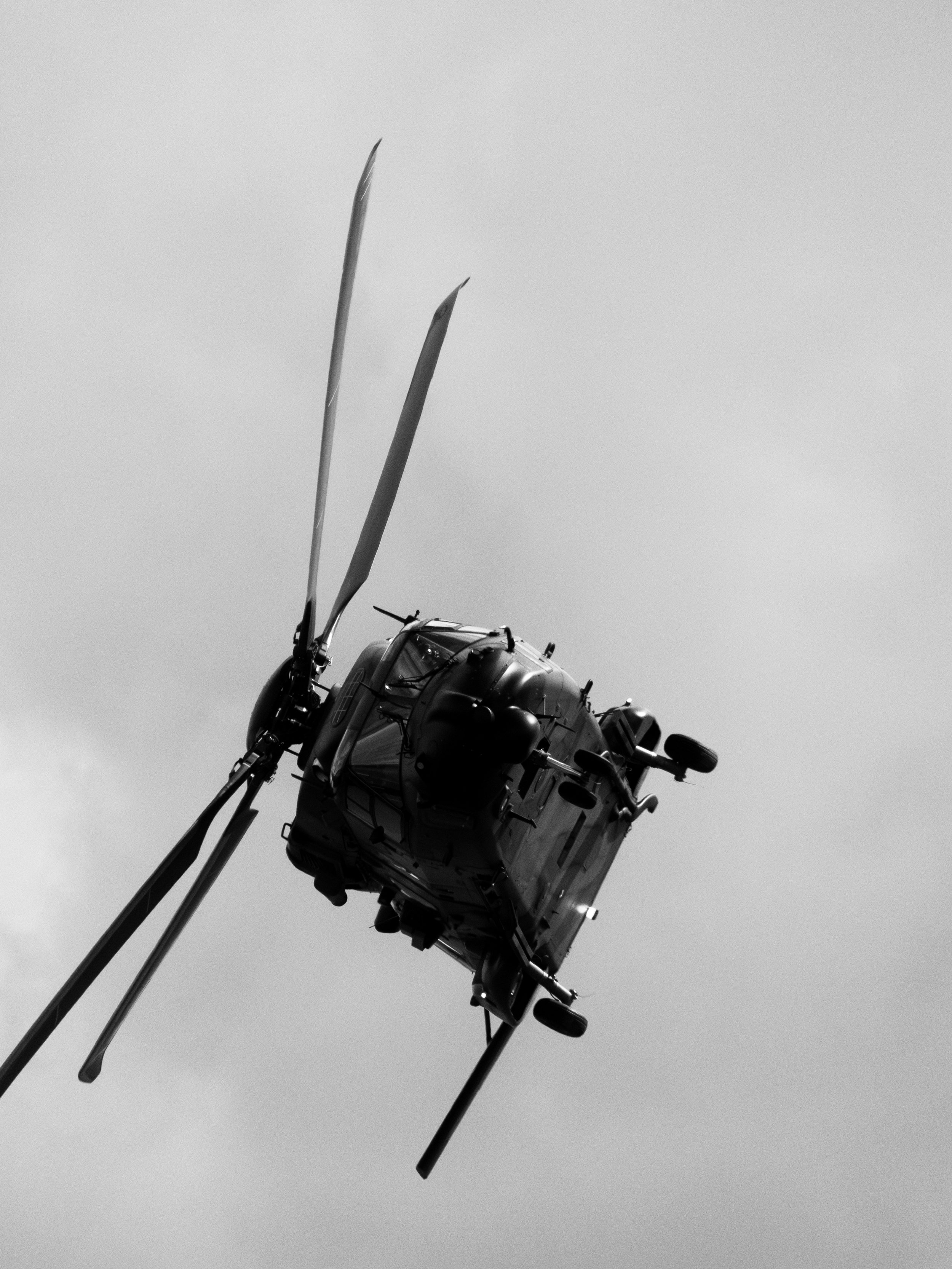 Un hélicoptère noir en vol vu de dessous contre un ciel gris
