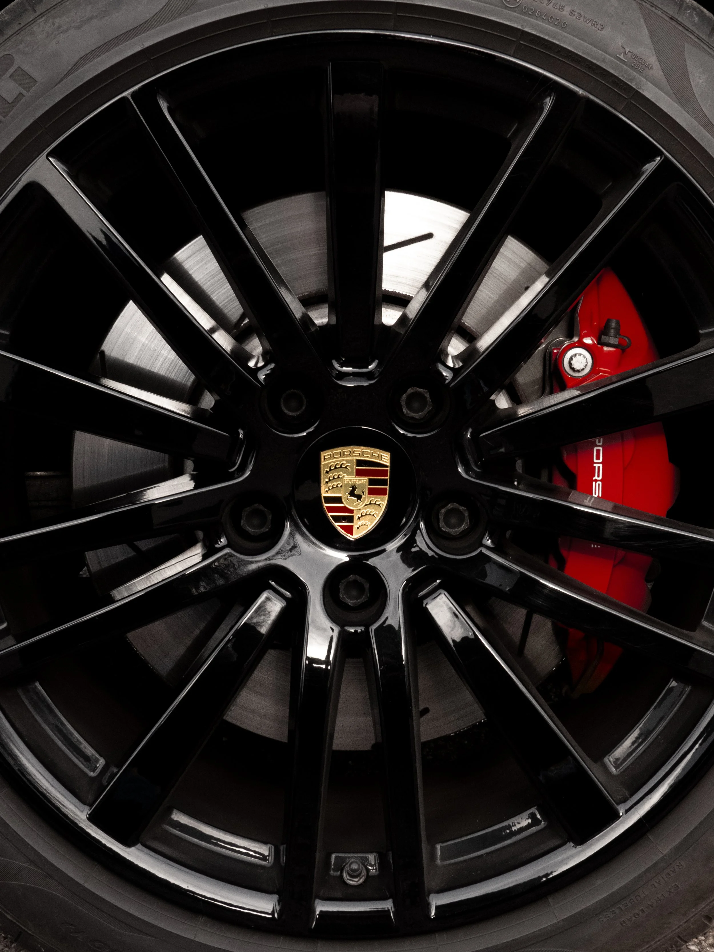 Vue d'une jante de roue de voiture noire avec le logo Porsche au centre, côté intérieur visible avec un étrier de frein rouge et un disque de frein en arrière.