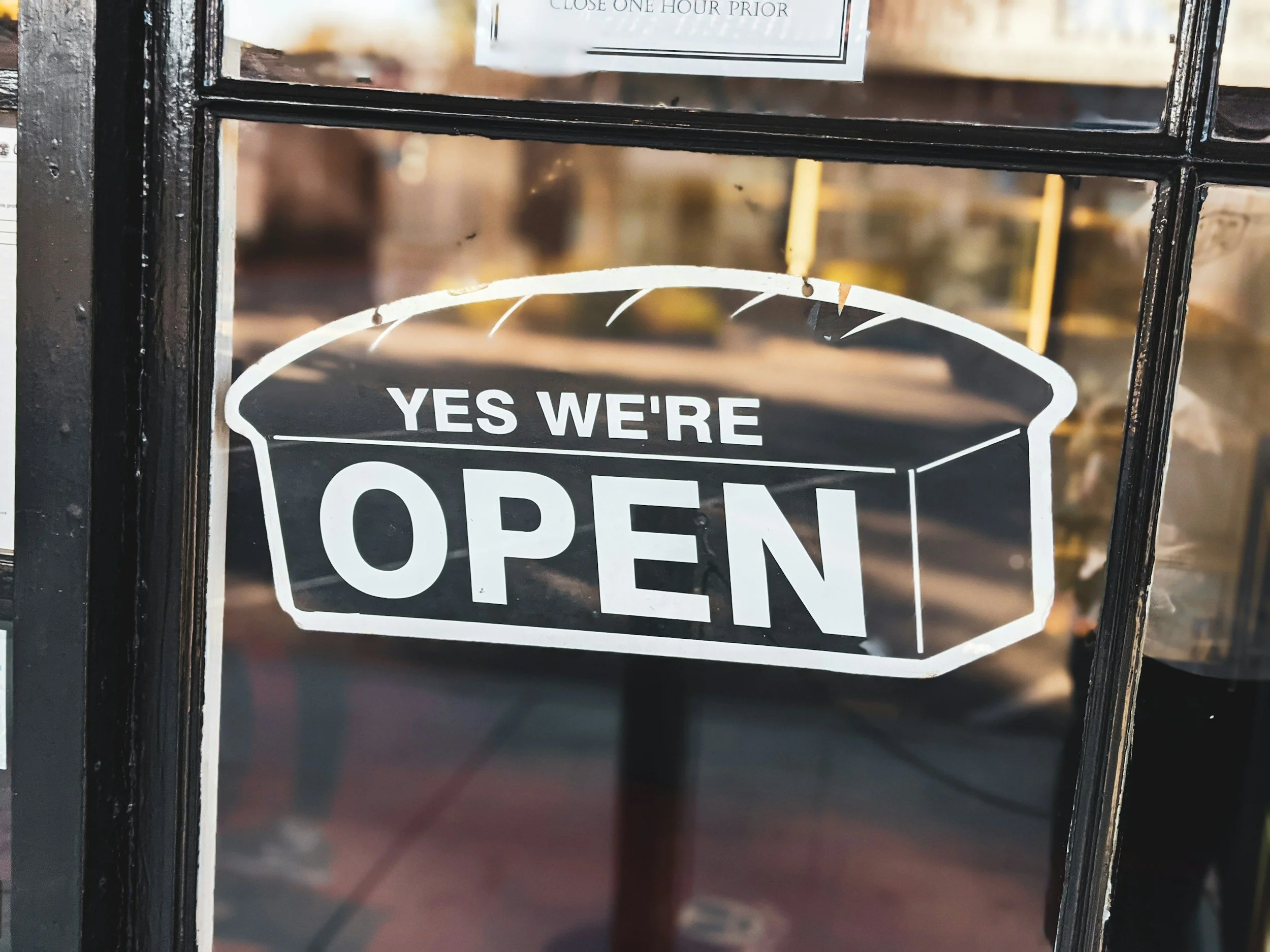 A black-framed glass sign with the word 'OPEN' visible, located outside a business.