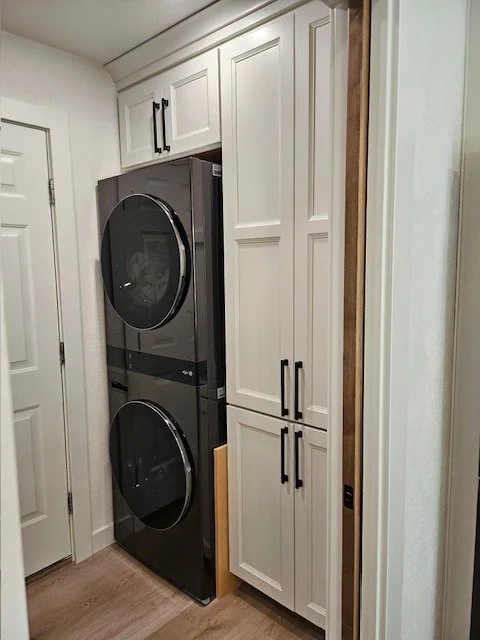 A laundry room with white cabinets and a stacked black washer and dryer.