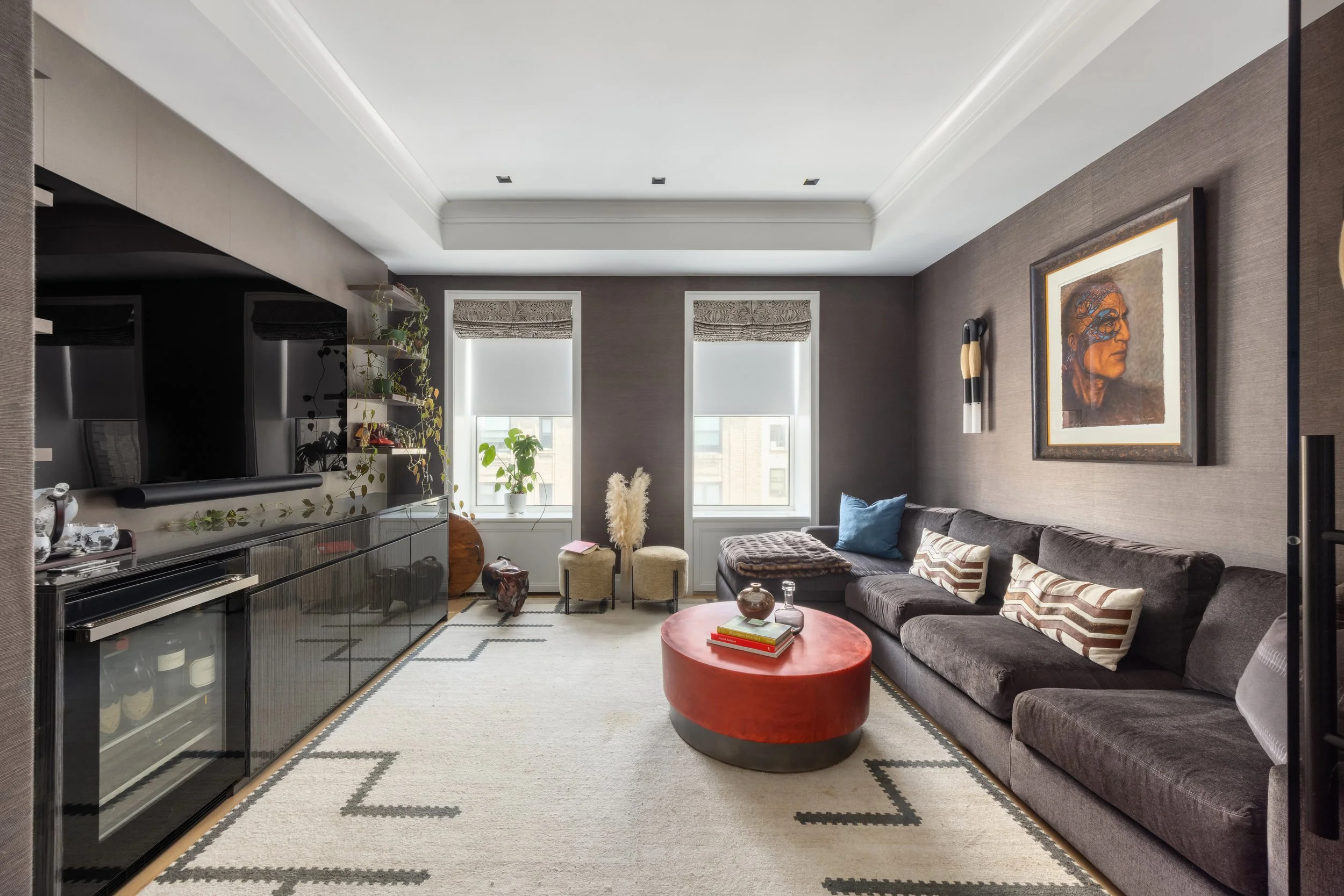 Living room with gray sofa, colorful pillows, wall art, dark shelving, and windows with blinds.