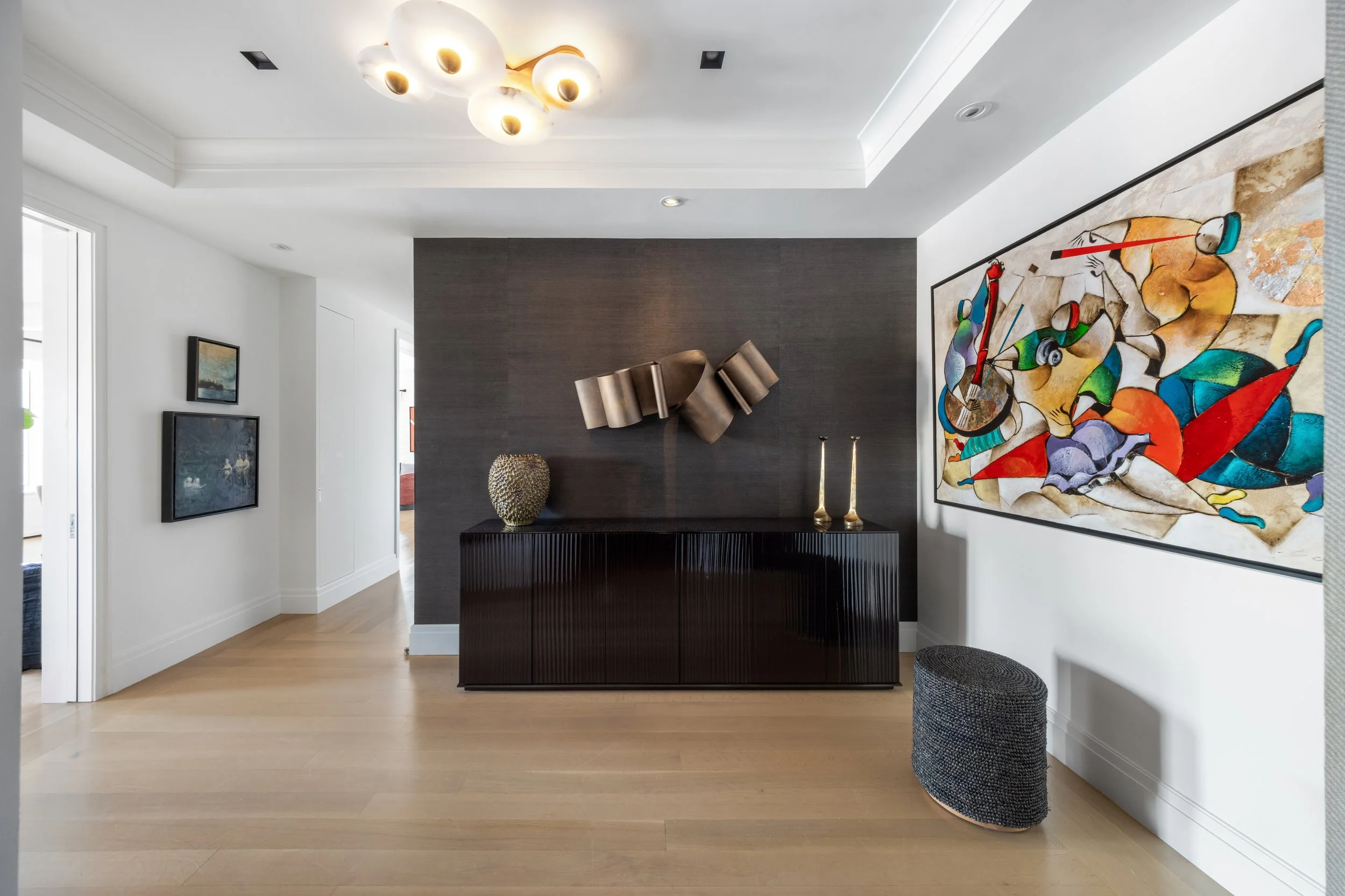 Interior of a modern living room with artwork, a dark textured accent wall, and a contemporary ceiling light fixture.