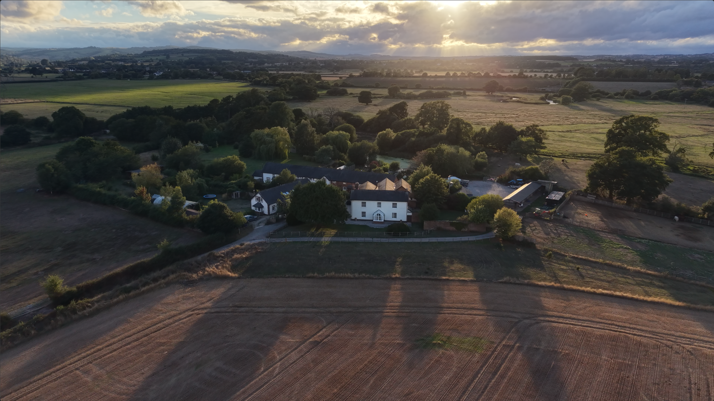 Aerial view of a rural farmhouse, barns, fields, and rolling countryside at sunset