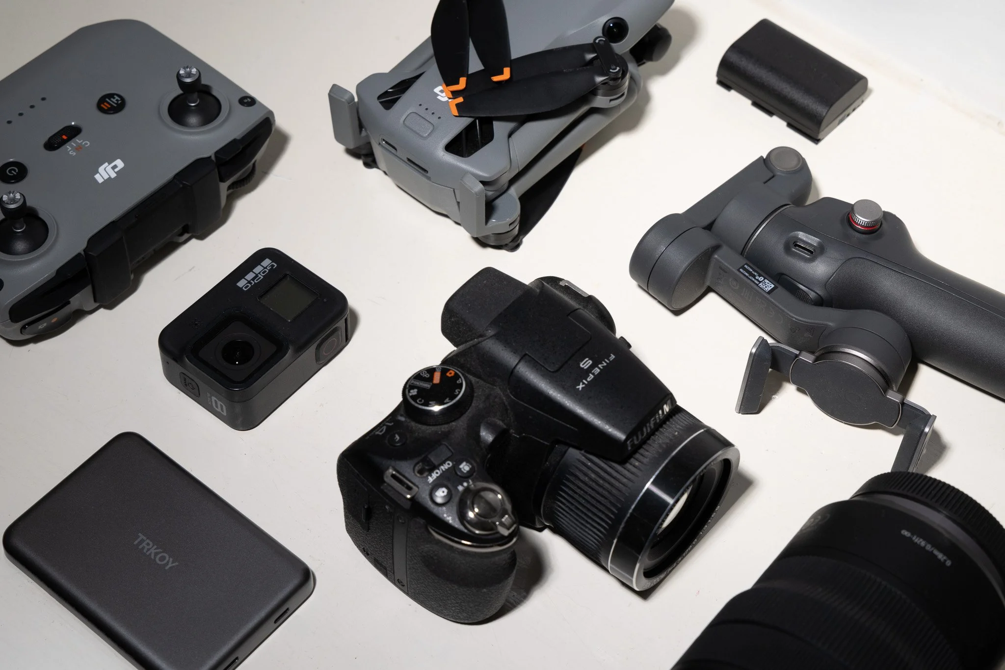 DJI drone, controllers, batteries, GoPro camera, Fujifilm camera, lenses, and accessories on a tabletop
