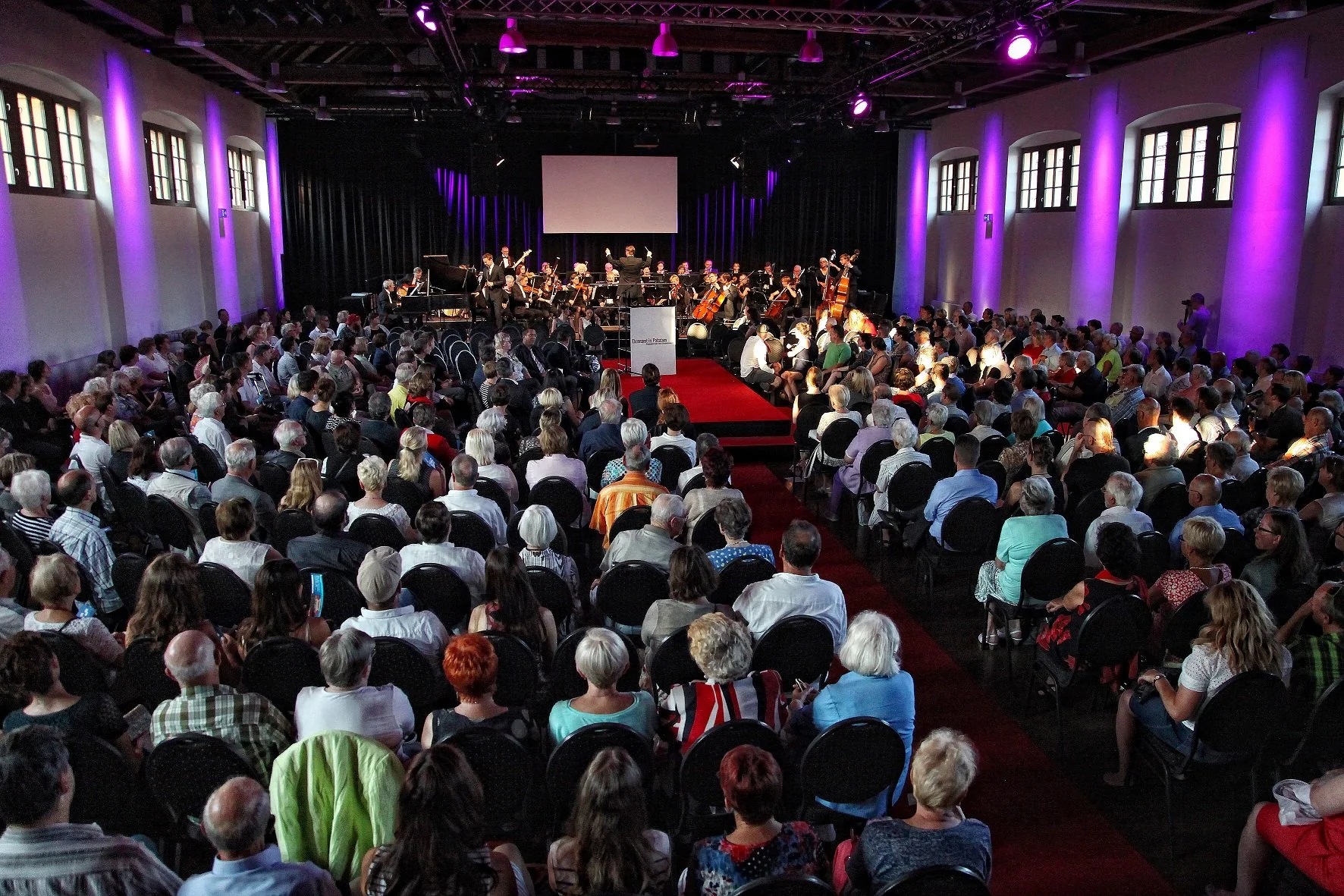 Konzertveranstaltung in der Schinkelhalle Potsdam mit Orchester, Publikum und farbiger Bühnenbeleuchtung.
