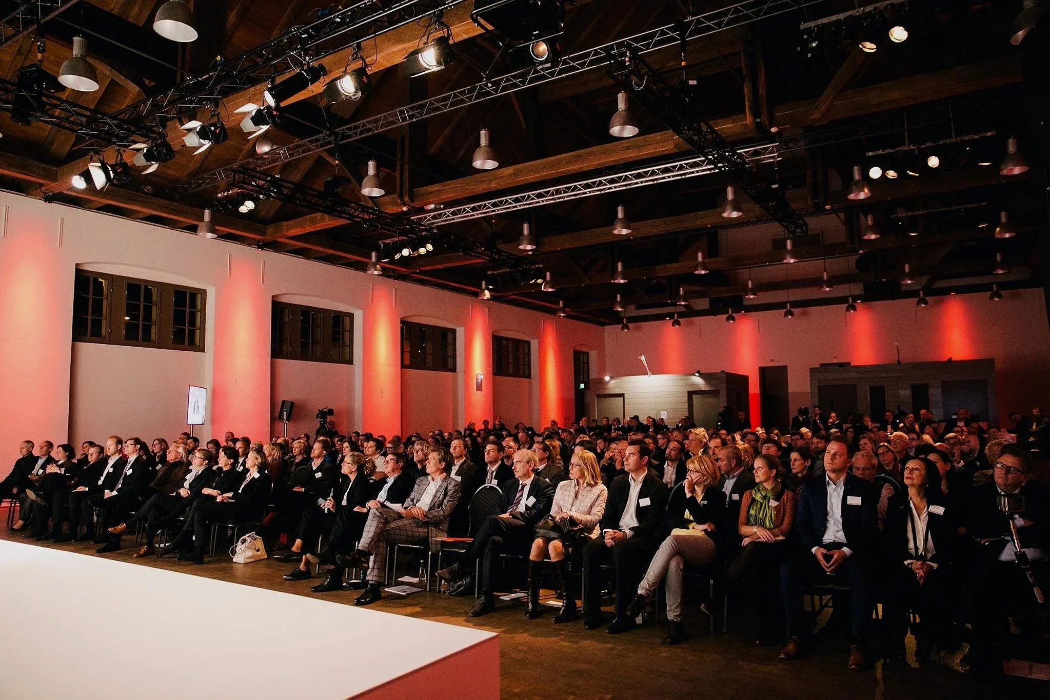 Schinkelhalle mit Gästen in Reihenbestuhlung und roter Ambientebeleuchtung