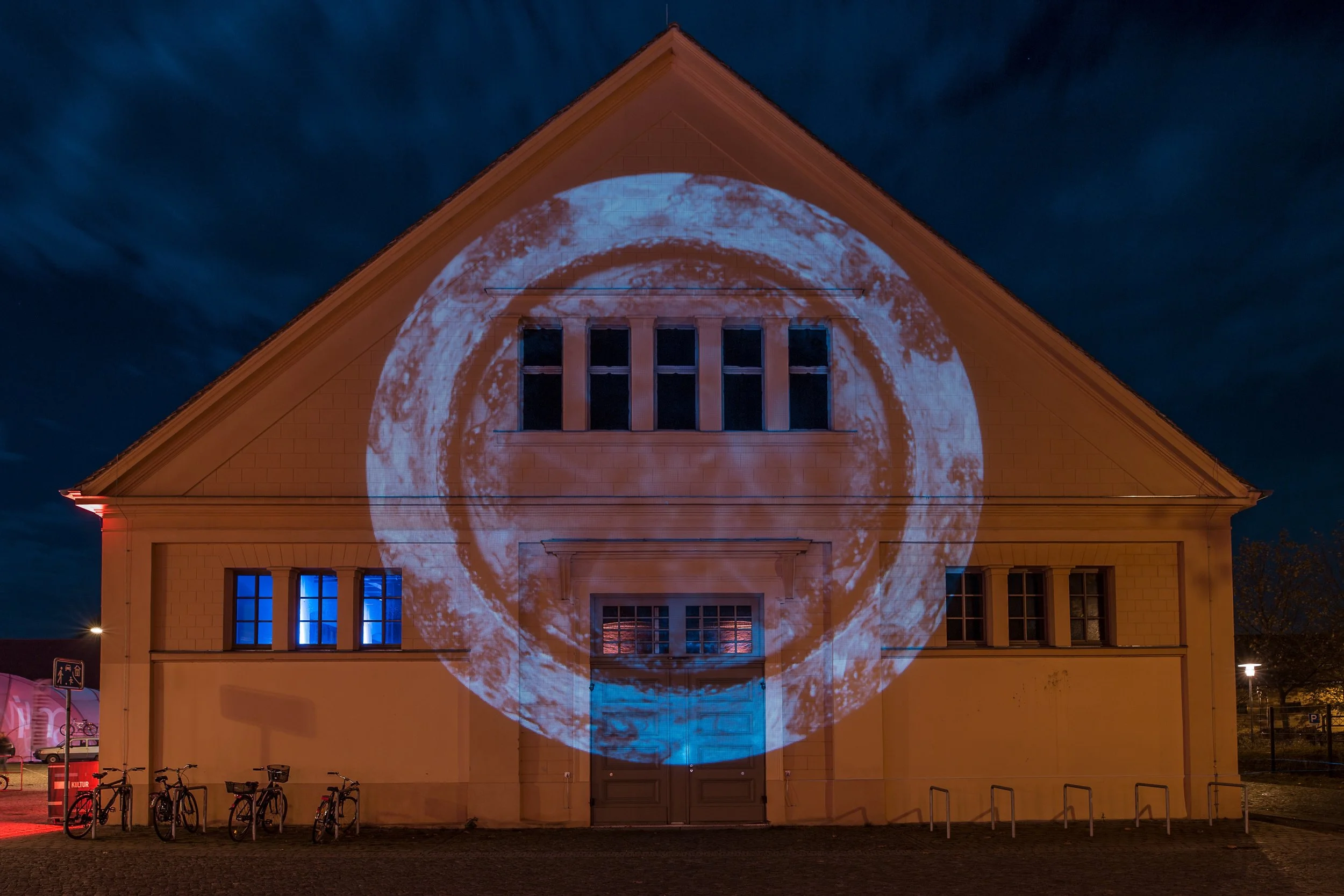 Illuminierte Außenfassade der Schinkelhalle Potsdam mit großflächiger Projektion auf dem Giebel.