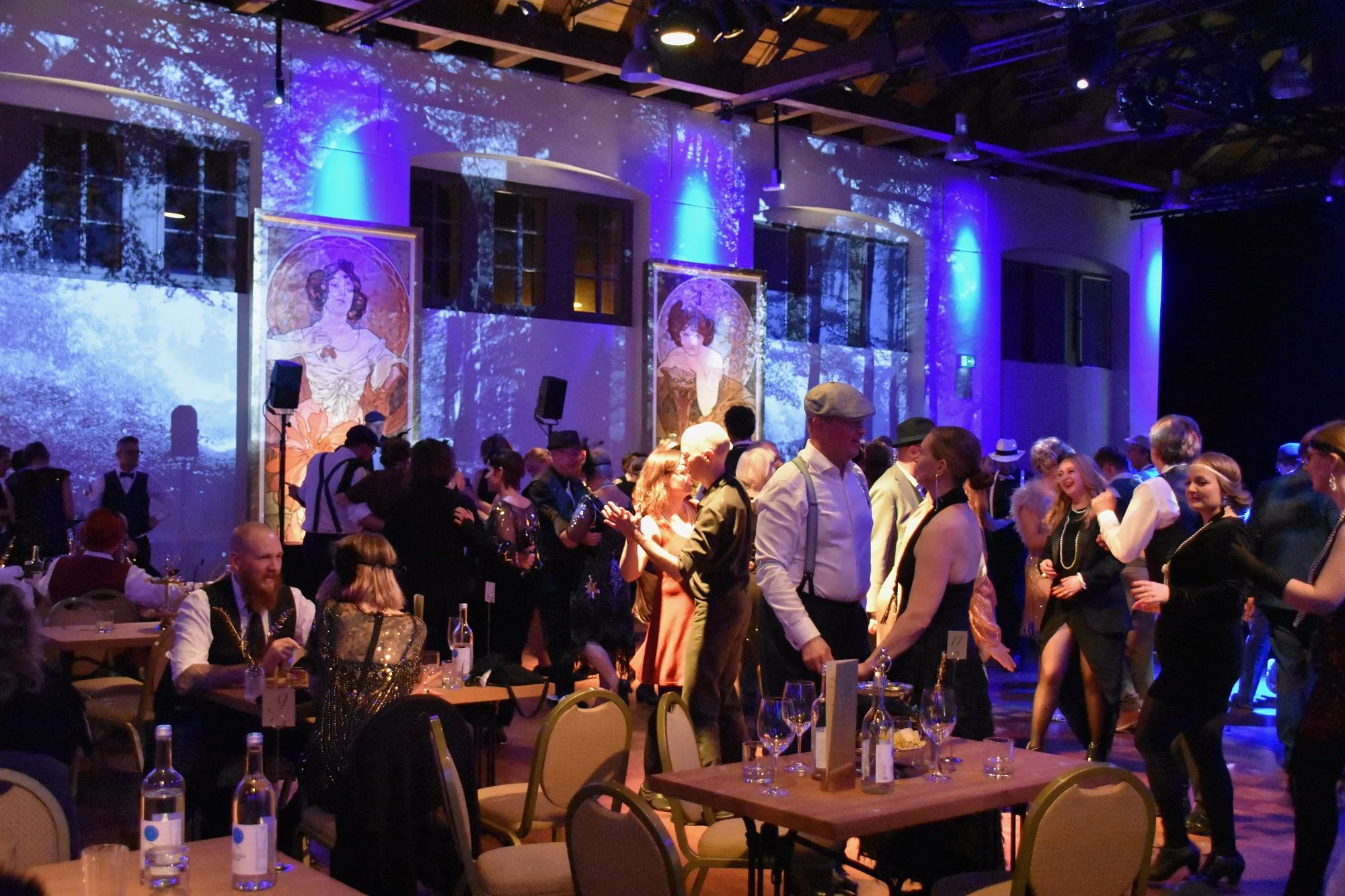 Menschen bei einer festlichen Party, die im Saal tanzen und sitzen, mit Bildern an der Wand und blauem Licht.