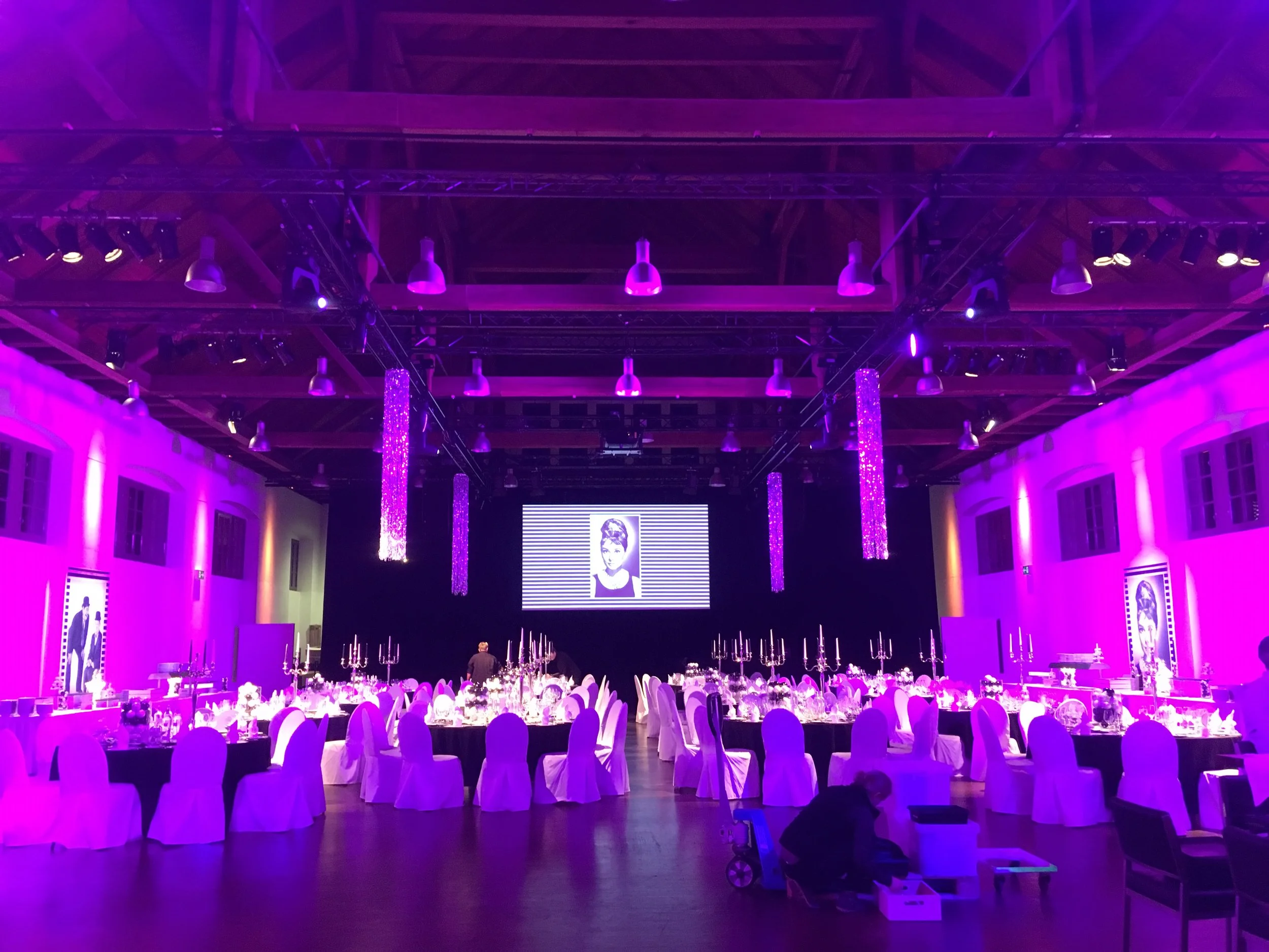 Galaabend in der Schinkelhalle Potsdam mit runden Tischen, Bühne und violetter Lichtinszenierung.