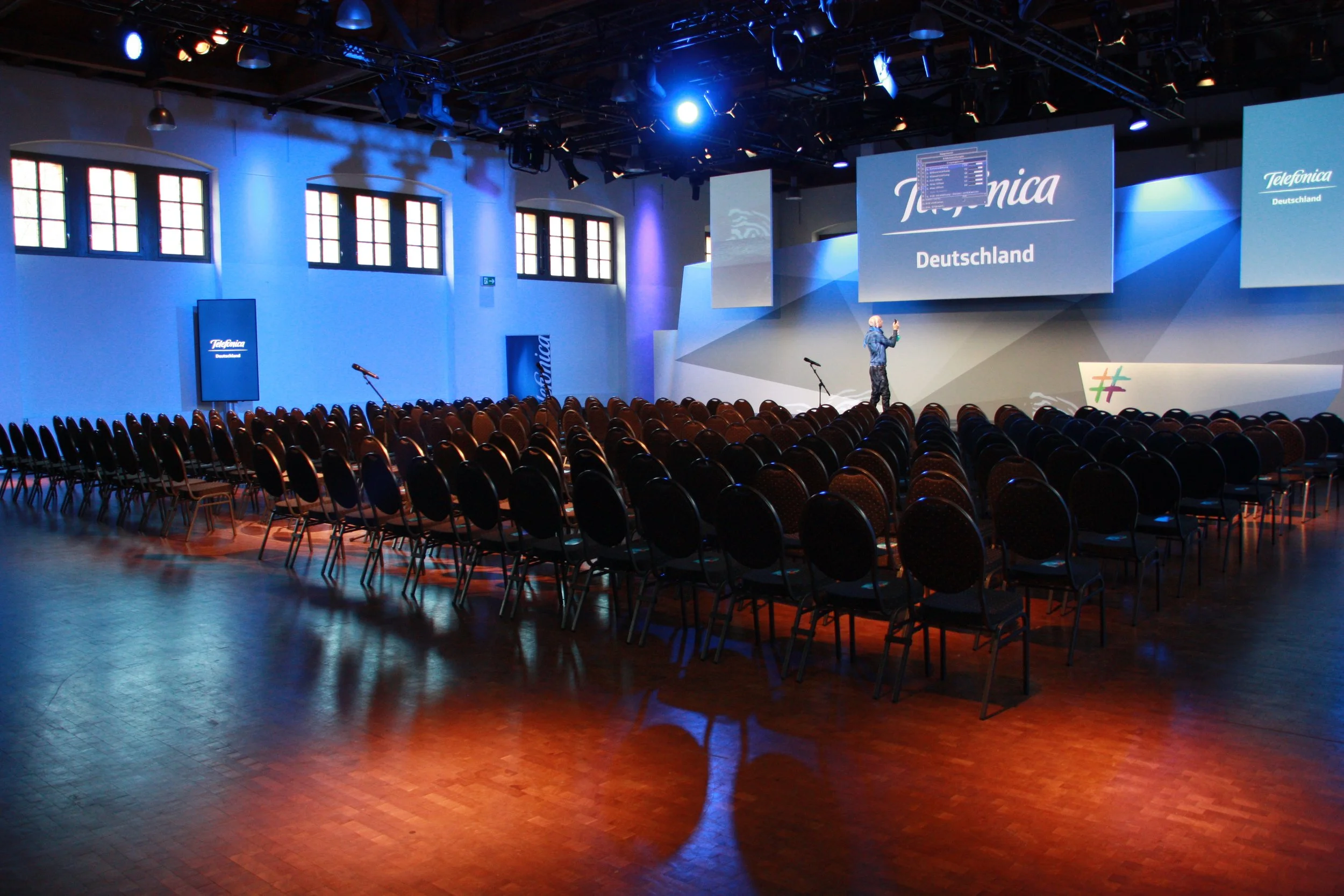 „Konferenz in der Schinkelhalle Potsdam mit Reihenbestuhlung, Bühne und großflächiger Präsentationstechnik.“