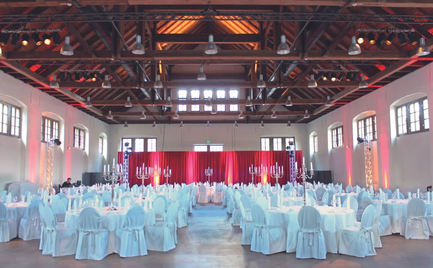 Festlich eingedeckte Schinkelhalle Potsdam für eine Hochzeit mit runden Tischen, Kronleuchtern und roter Stoffinszenierung.