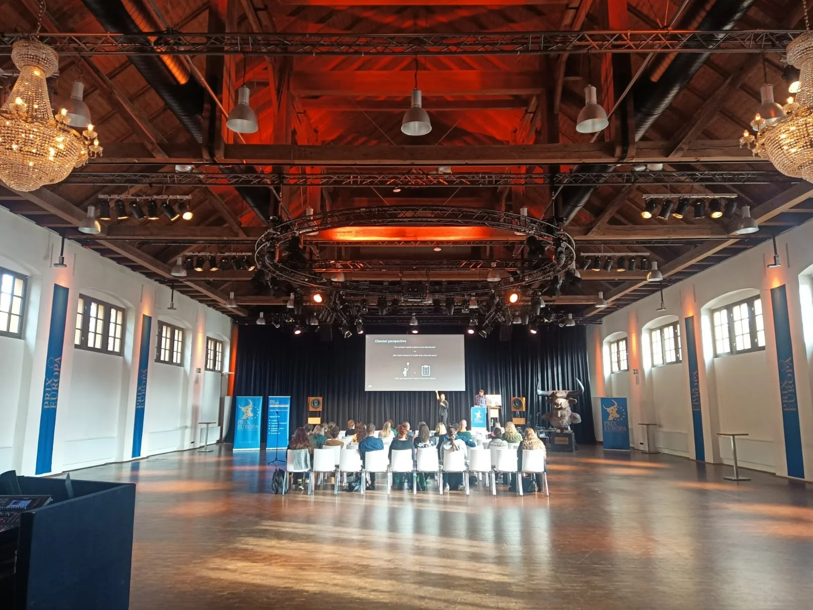 „Tagungsveranstaltung in der Schinkelhalle Potsdam mit Bühne, Präsentationsfläche und Bestuhlung im offenen Raum.“