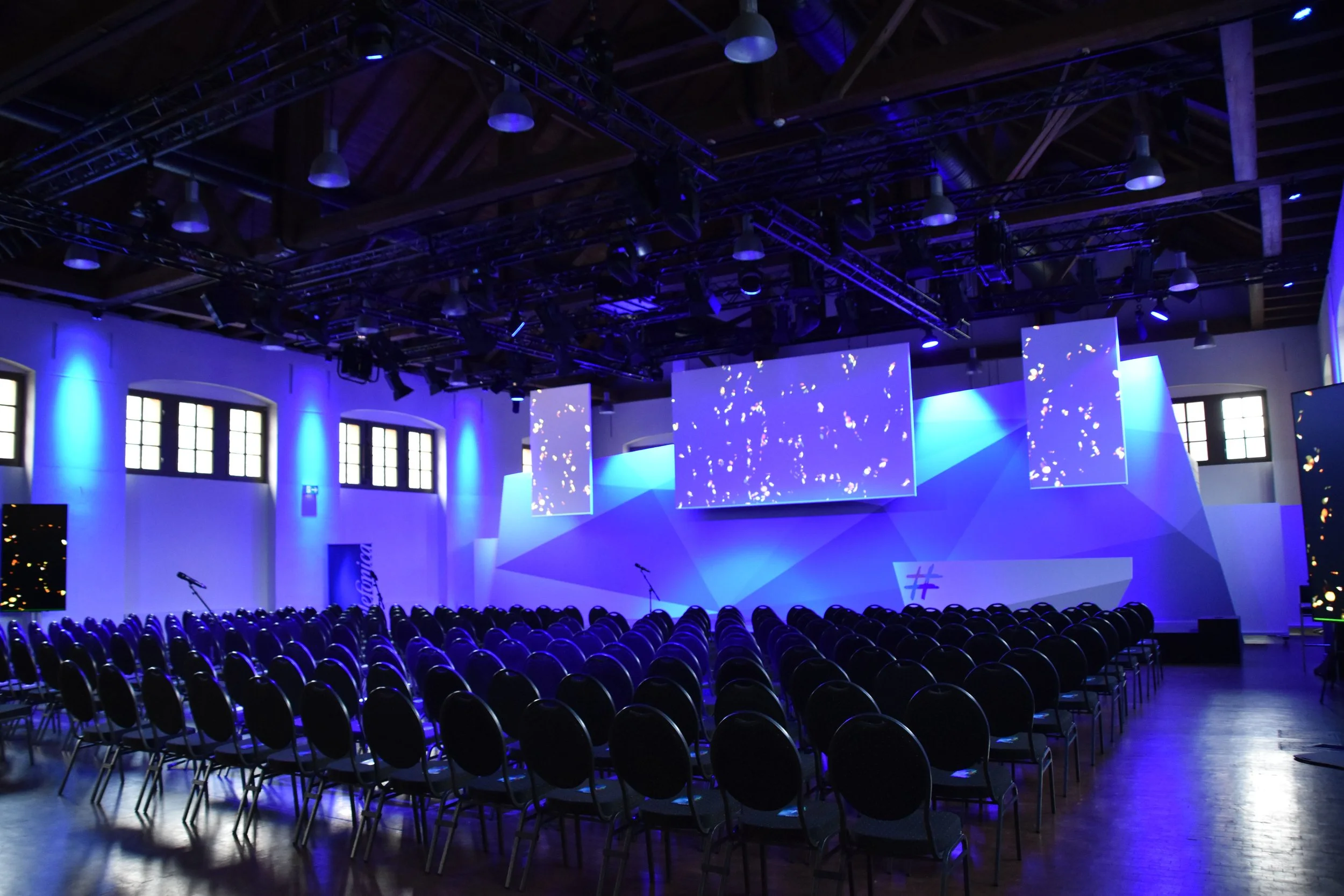 Veranstaltung in der Schinkelhalle Potsdam mit Reihenbestuhlung, großer Projektionsfläche und blauer Lichtinszenierung.