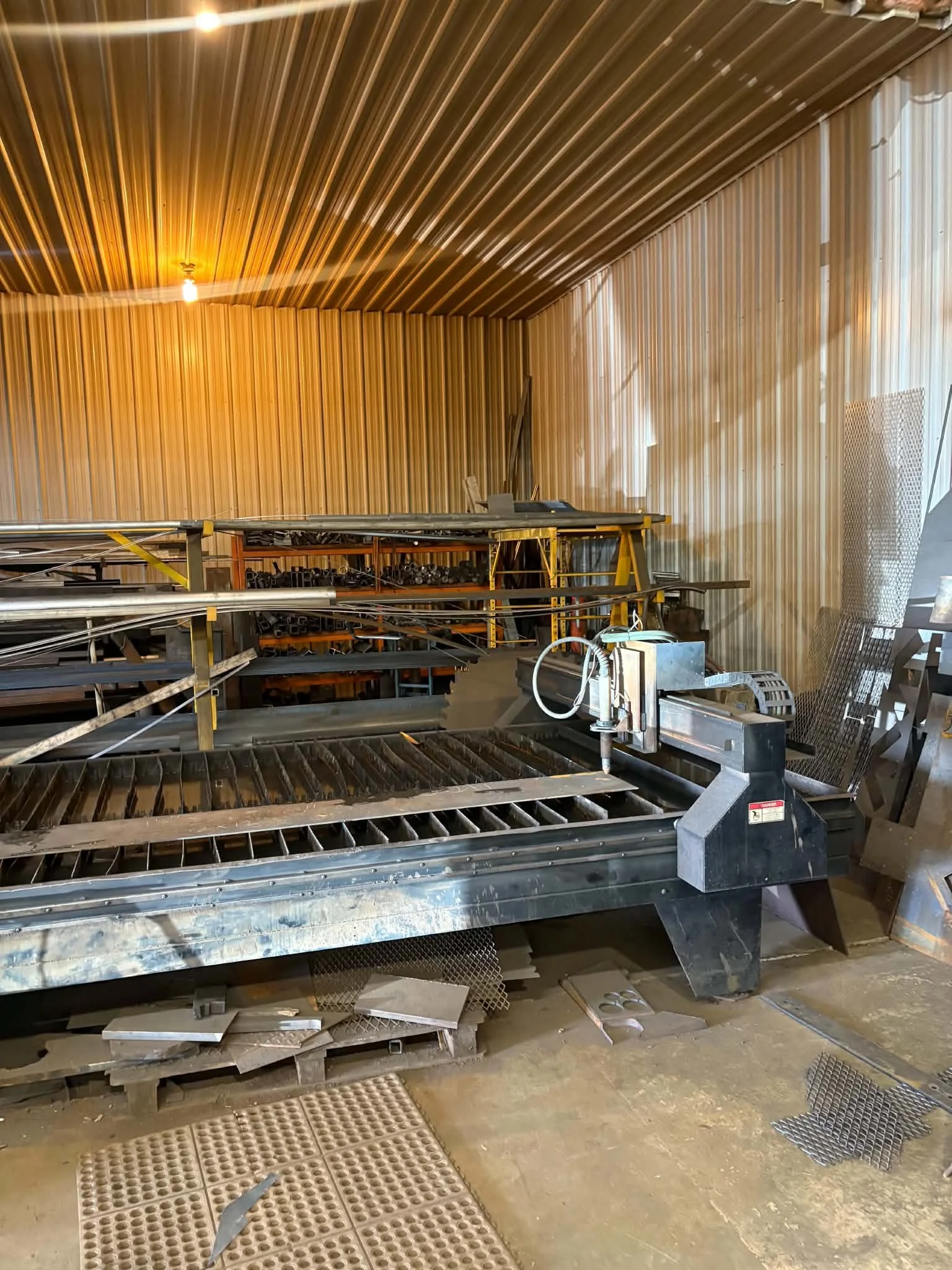 Industrial workspace with metal shelves, tools, and miscellaneous metal parts, with corrugated metal walls and a concrete floor.