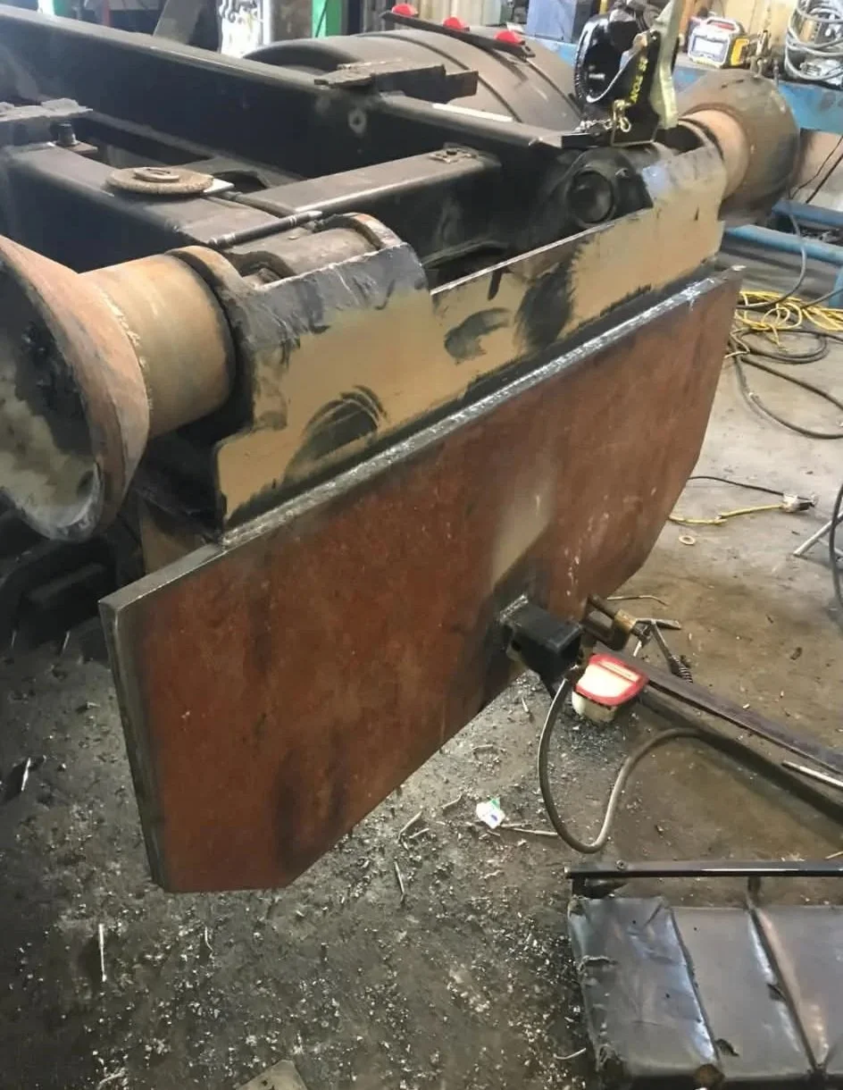 A large metal object, possibly part of a machine or industrial equipment, is being worked on in a workshop. It has a rusty surface with some freshly welded or assembled sections. Tools and electrical cords are visible around it.