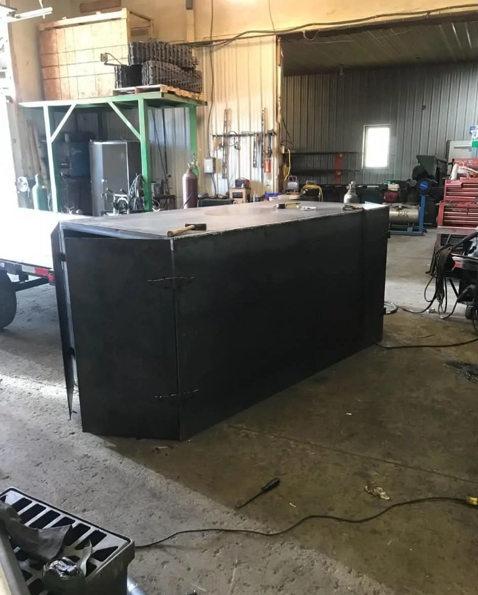A large black metal counter with tools on top in a workshop with industrial shelves, equipment, and tools in the background.