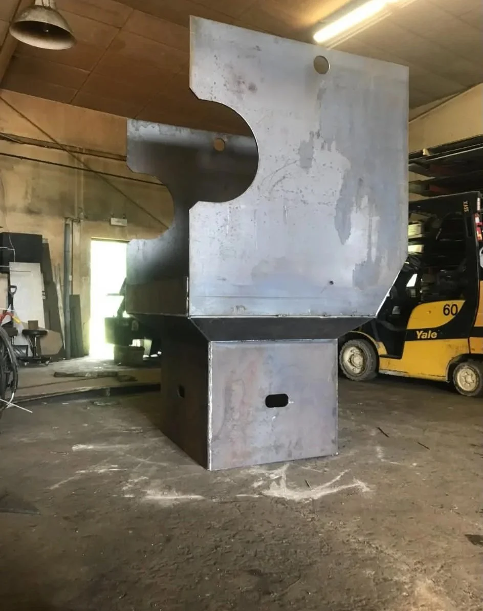 Large metal industrial structure with curved cutout and rectangular base in a warehouse.