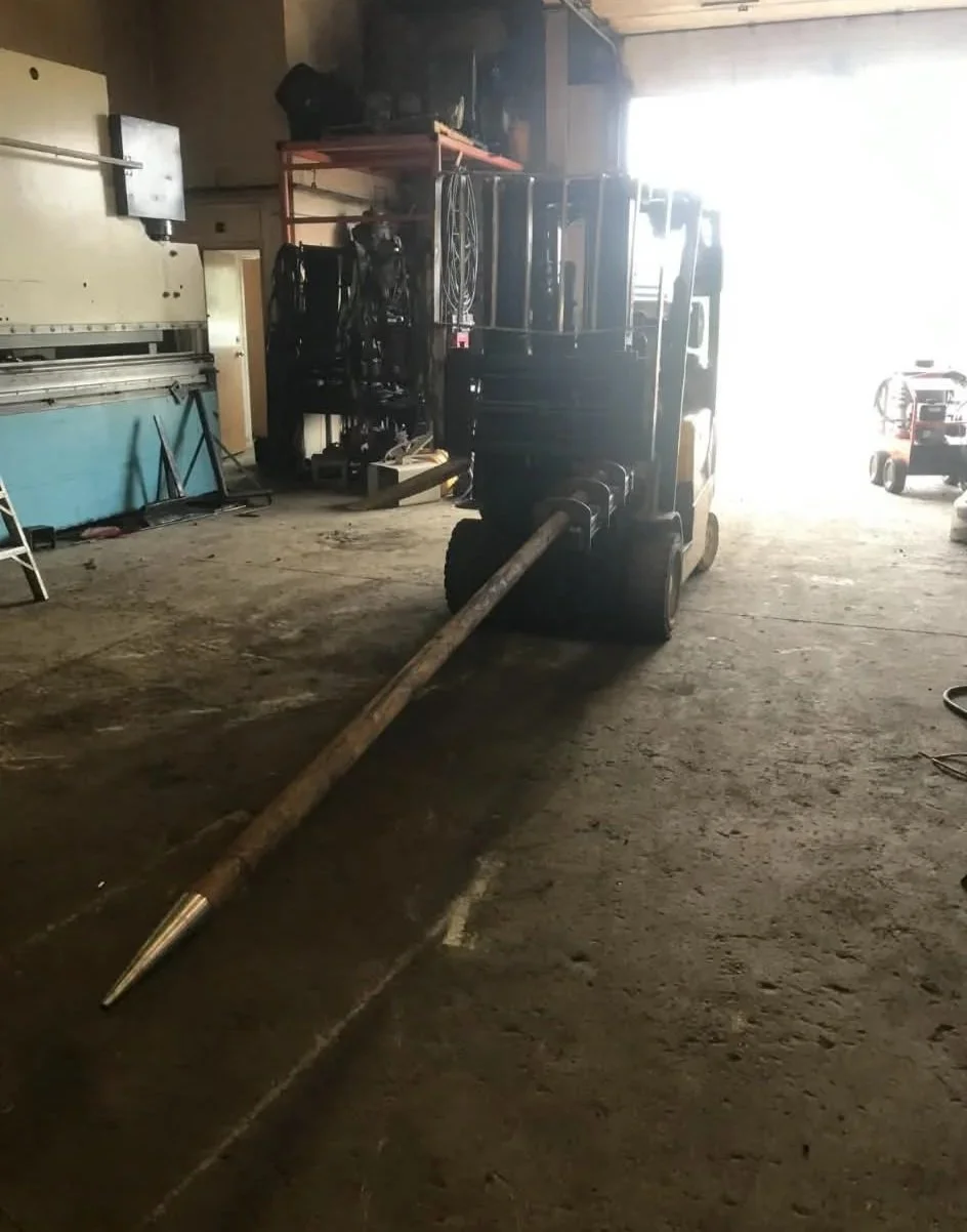 A forklift with a long pole attached, inside a warehouse with tools and equipment around.