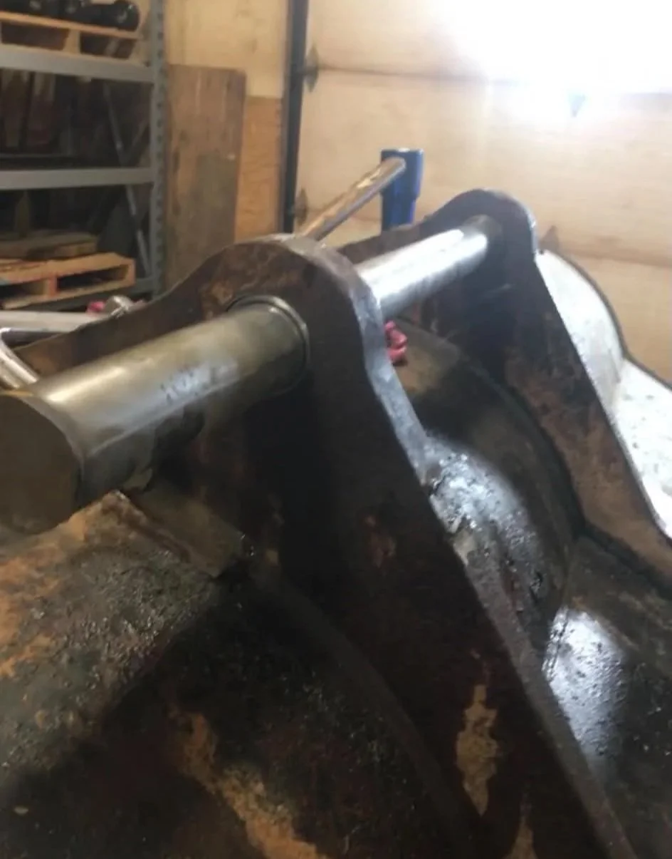 Close-up of a mechanical bucket attachment in a workshop, with metal bars and tools in the background.