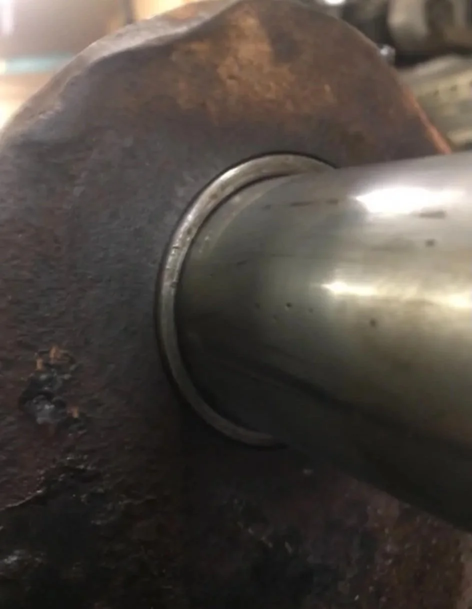 Close-up of a worn metal shaft with a shiny, smooth cylindrical extension, mounted on a rough, rusted surface.