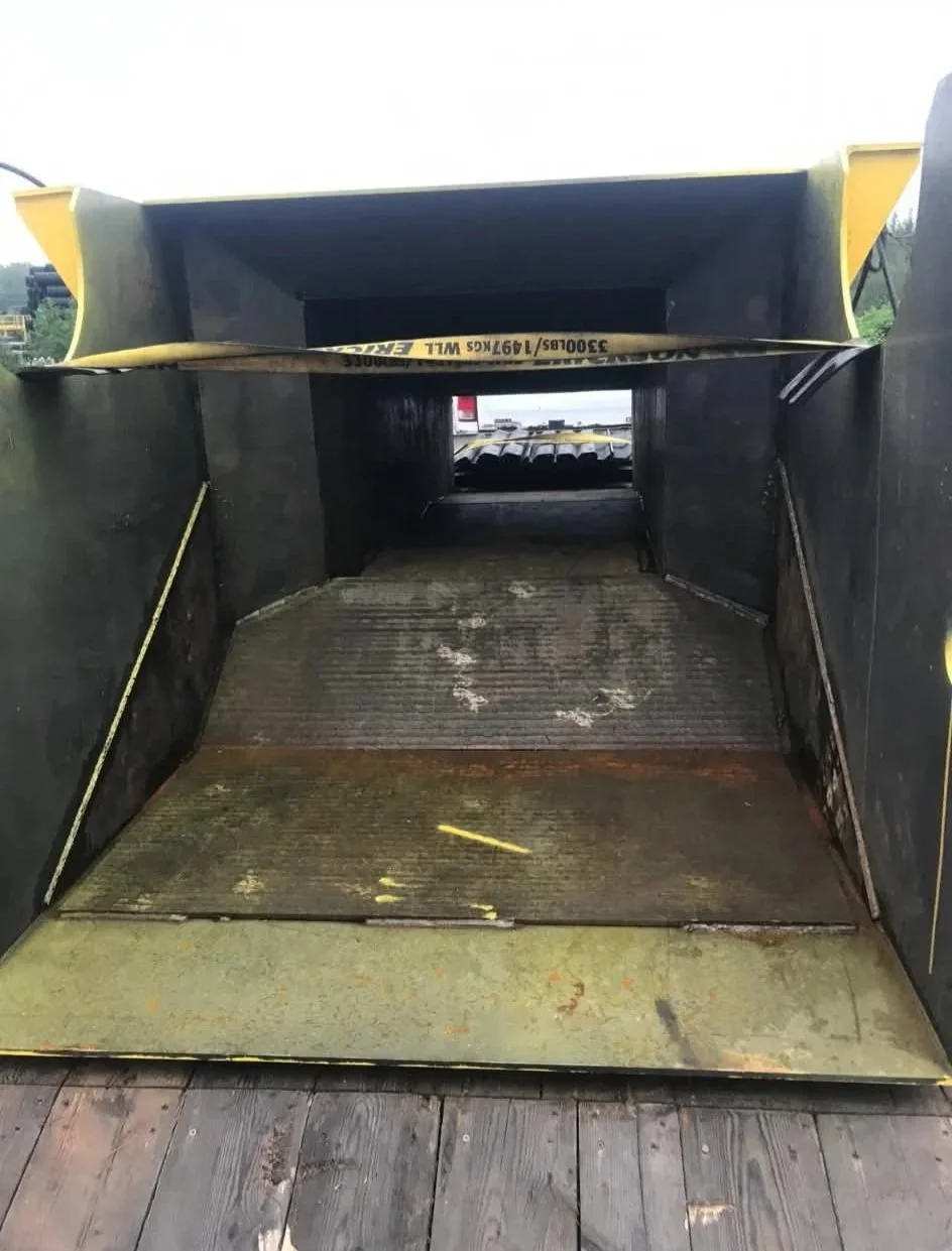 Large black metal equipment part with a grated ramp at the front, inside a storage or industrial area.