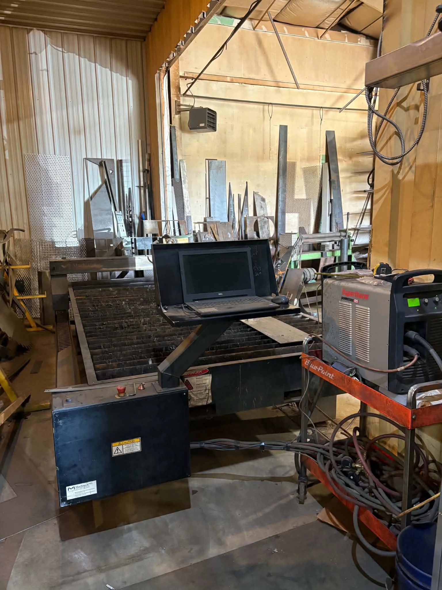Warehouse or workshop with various metal tools, equipment, and machinery, including a metal frame, a laptop, and welding machines.