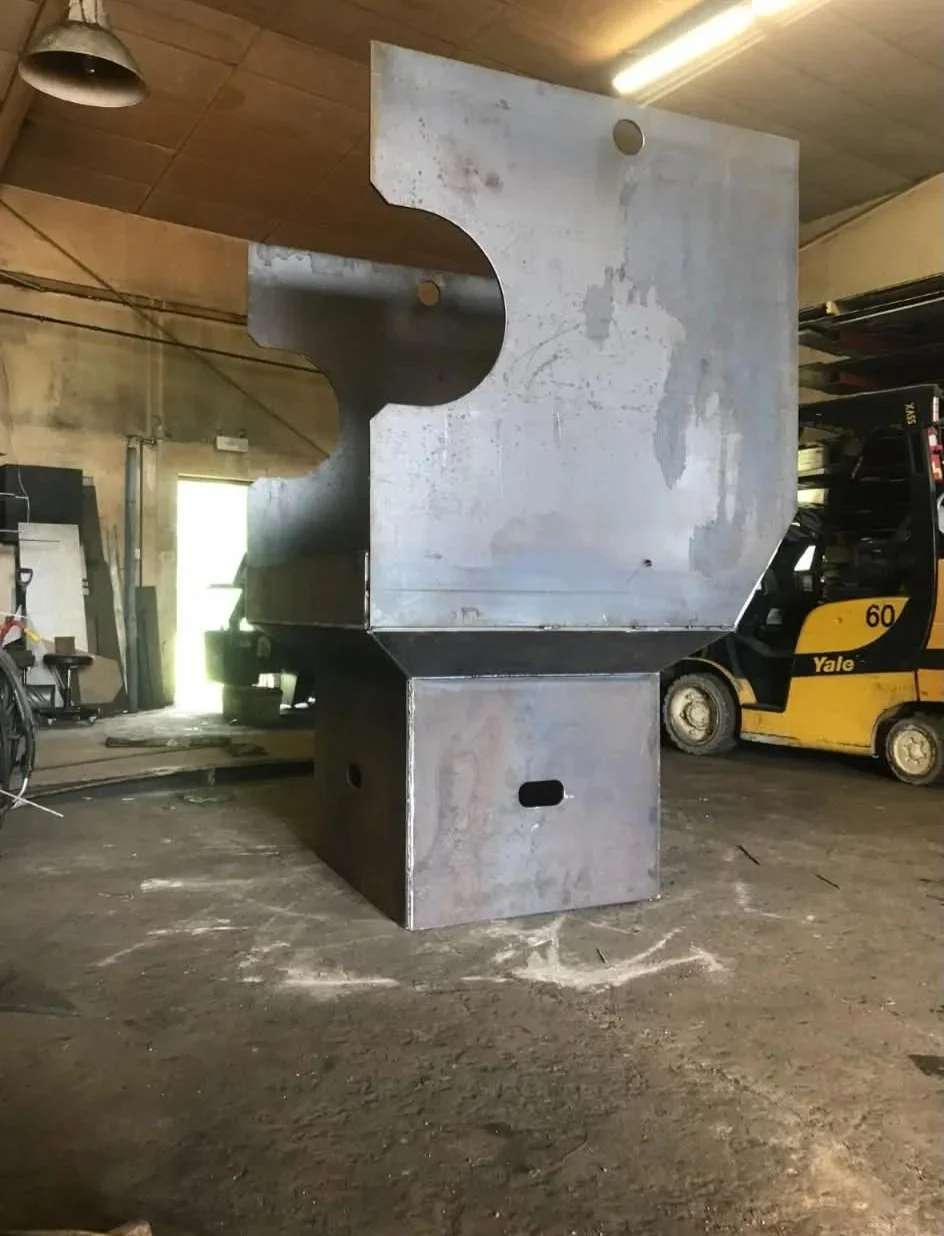 Large metal industrial machine with a cylindrical opening on one side, located in a warehouse with a forklift and other equipment nearby.