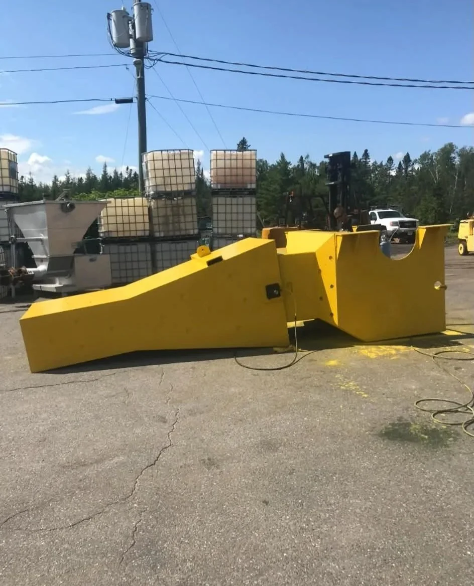 Large yellow industrial equipment on cracked asphalt ground, with large tanks and machinery in the background, outdoors under a blue sky.
