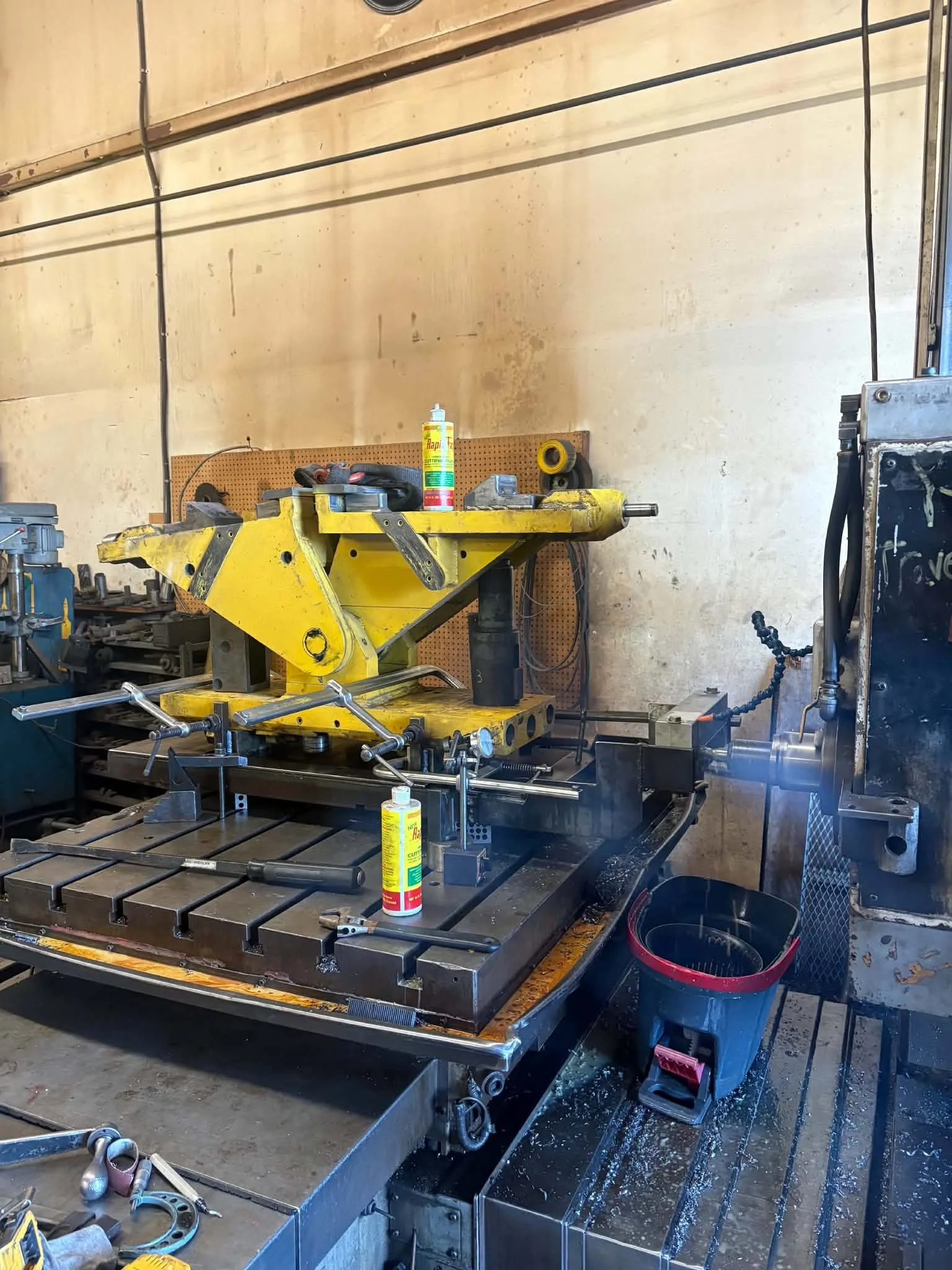Workshop with yellow vise, workbench, various tools, and containers in a garage or factory setting.
