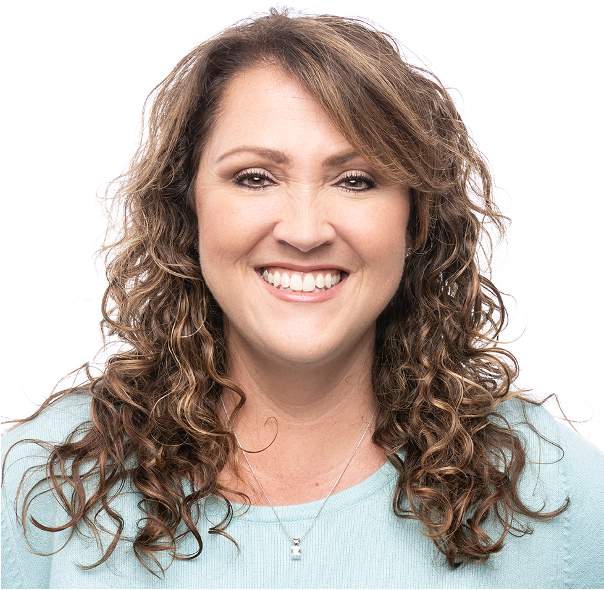 A woman with curly brown hair smiling, wearing a light blue top and a silver necklace, against a white background.