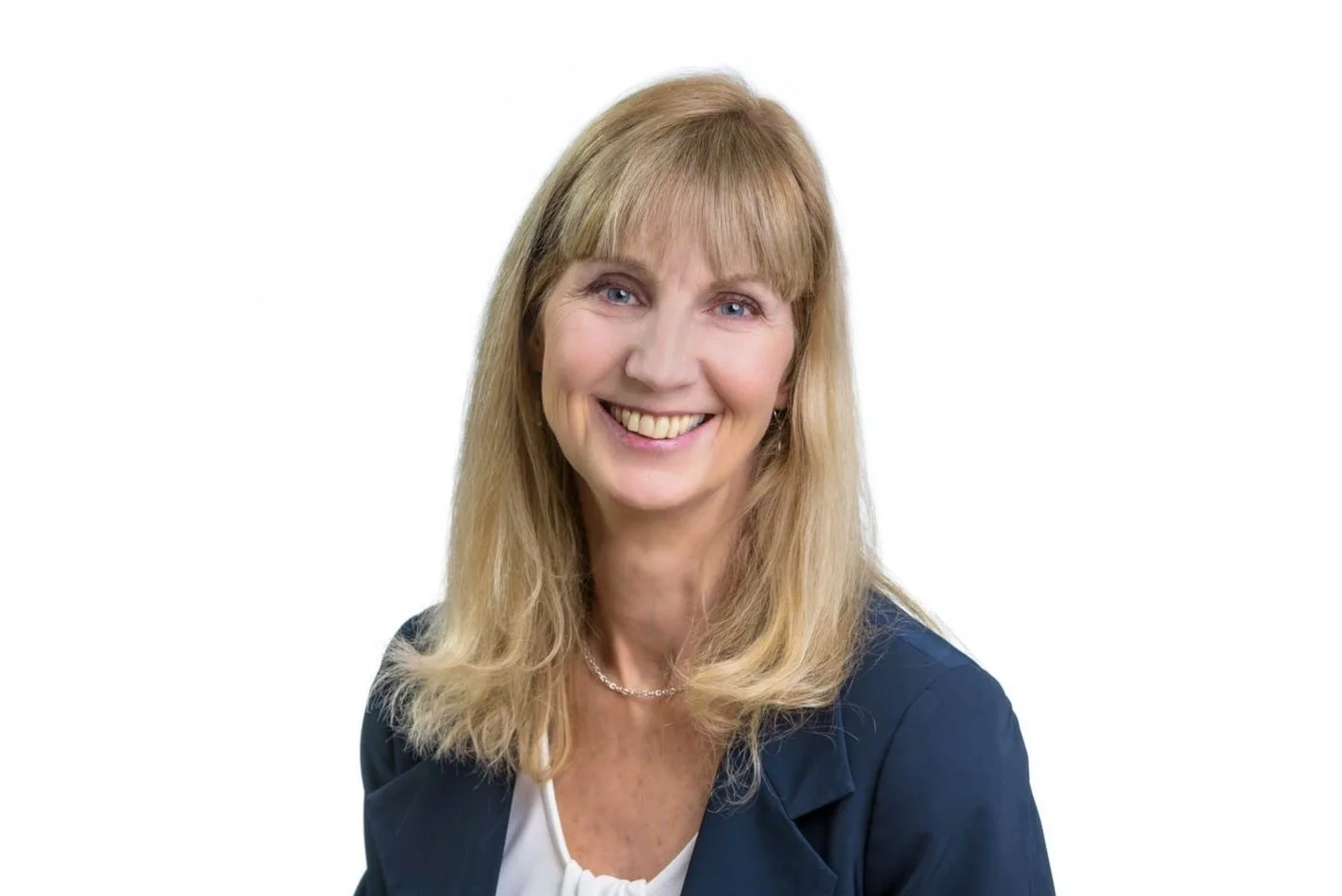 Portrait of a smiling woman with blonde hair, wearing a navy blue blazer and white top against a white background.