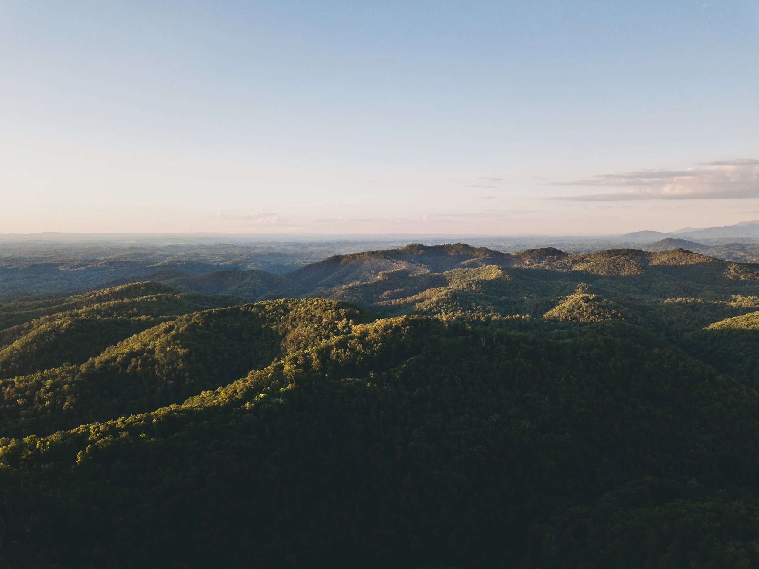 Landscape of rolling green hills under a clear blue sky with some clouds in the distance.