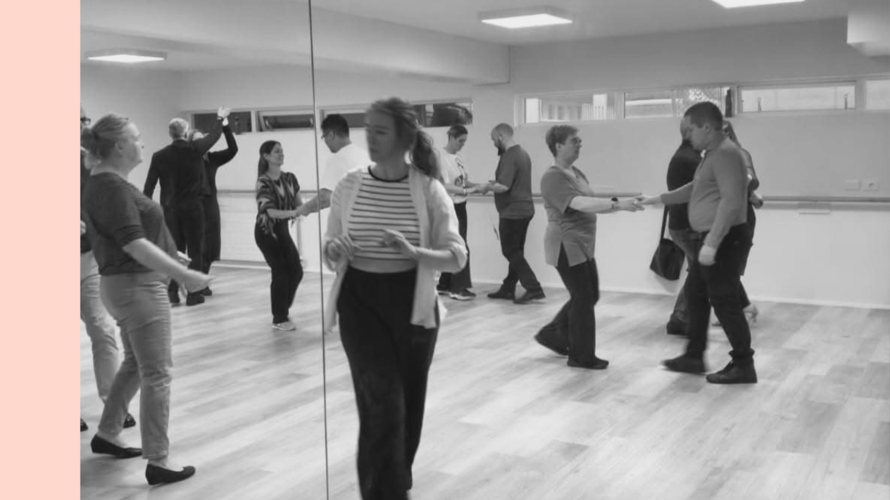 People dancing in a dance studio with mirrors on the wall, holding hands and practicing dance steps.