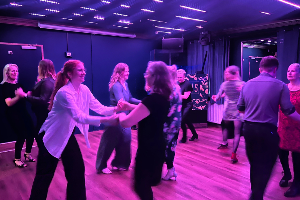 People dancing and socializing in a dimly lit nightclub with purple LED lighting on the ceiling.